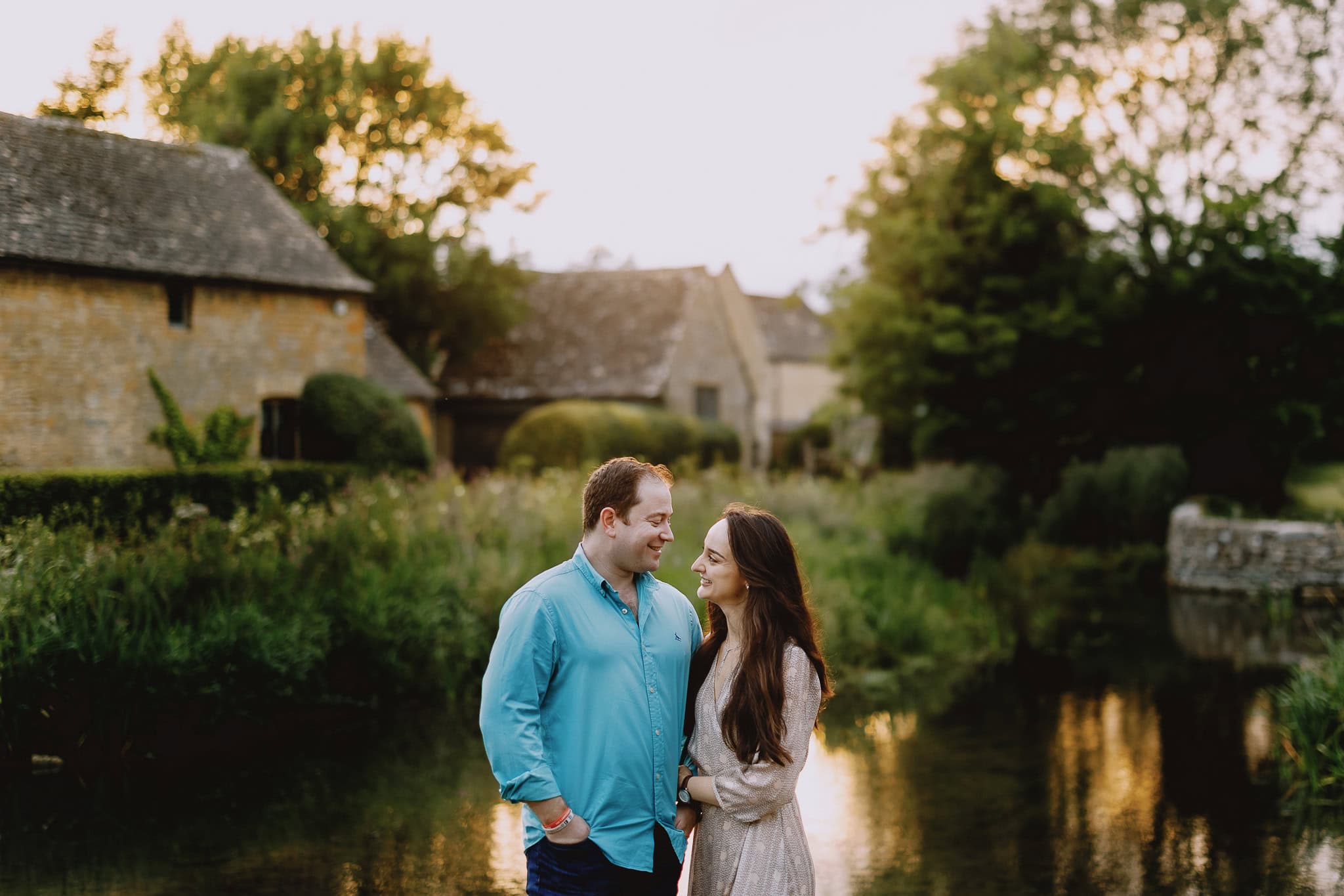 Couple smiling during pre-wedding shoot by river, Cotswolds.