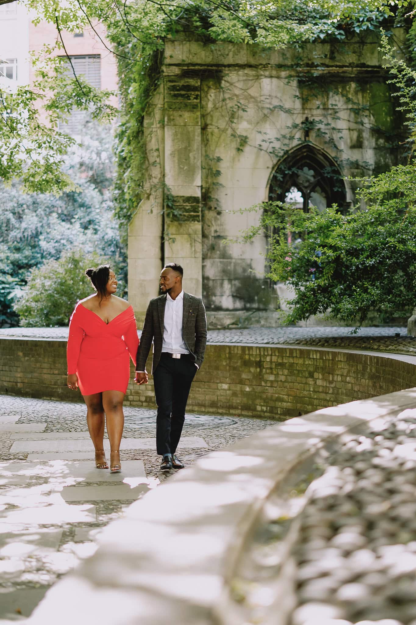 Couple holding hands during their pre-wedding shoot in a garden with stone architecture.