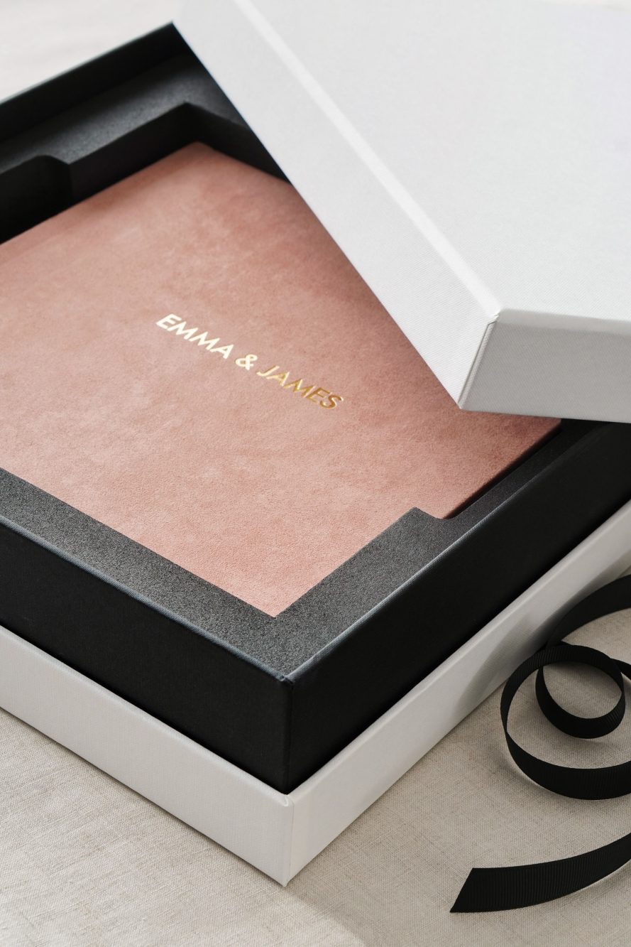 A pink cover wedding album in a white box with black ribbon.