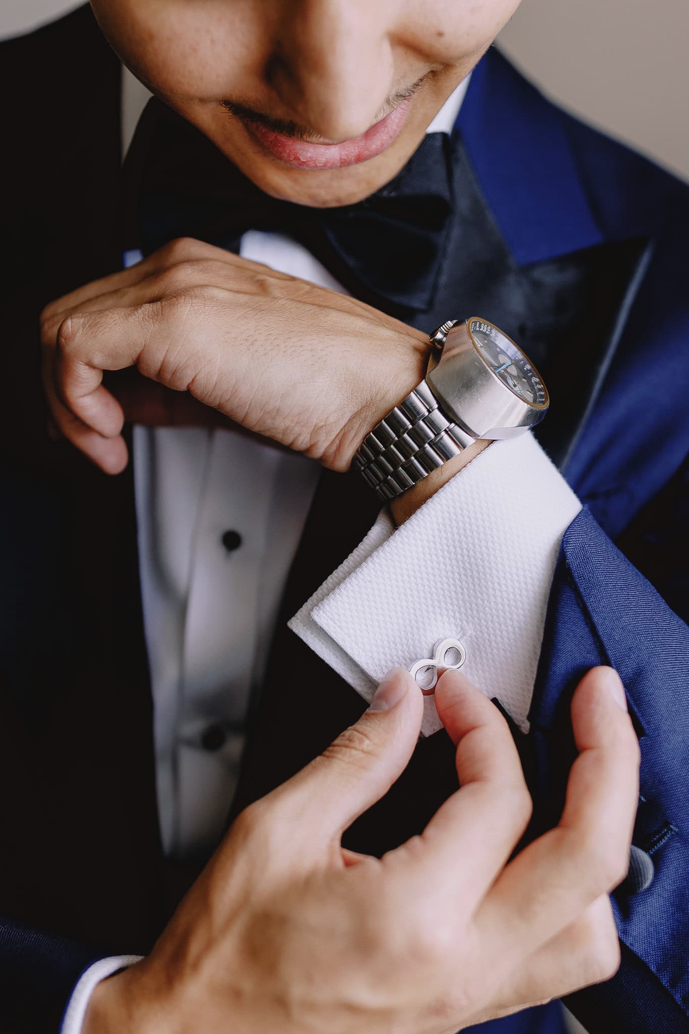 Groom adjusts cufflink wearing a blue tuxedo and watch, wedding photography portfolio.