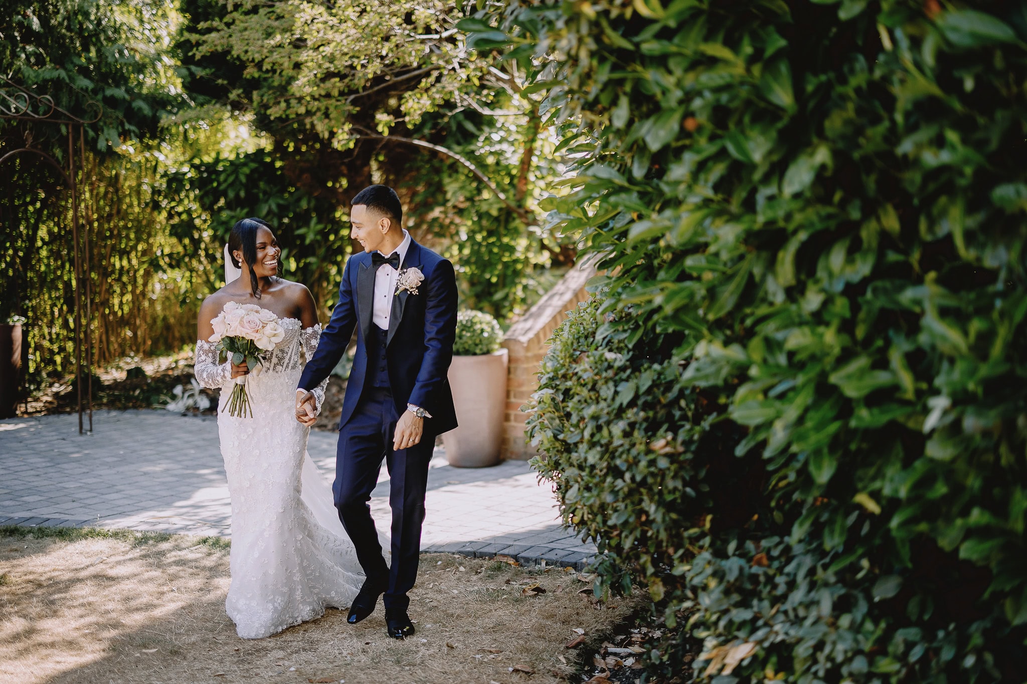 Wedding photography portfolio: Bride and groom walking hand-in-hand in a garden, smiling at each other.