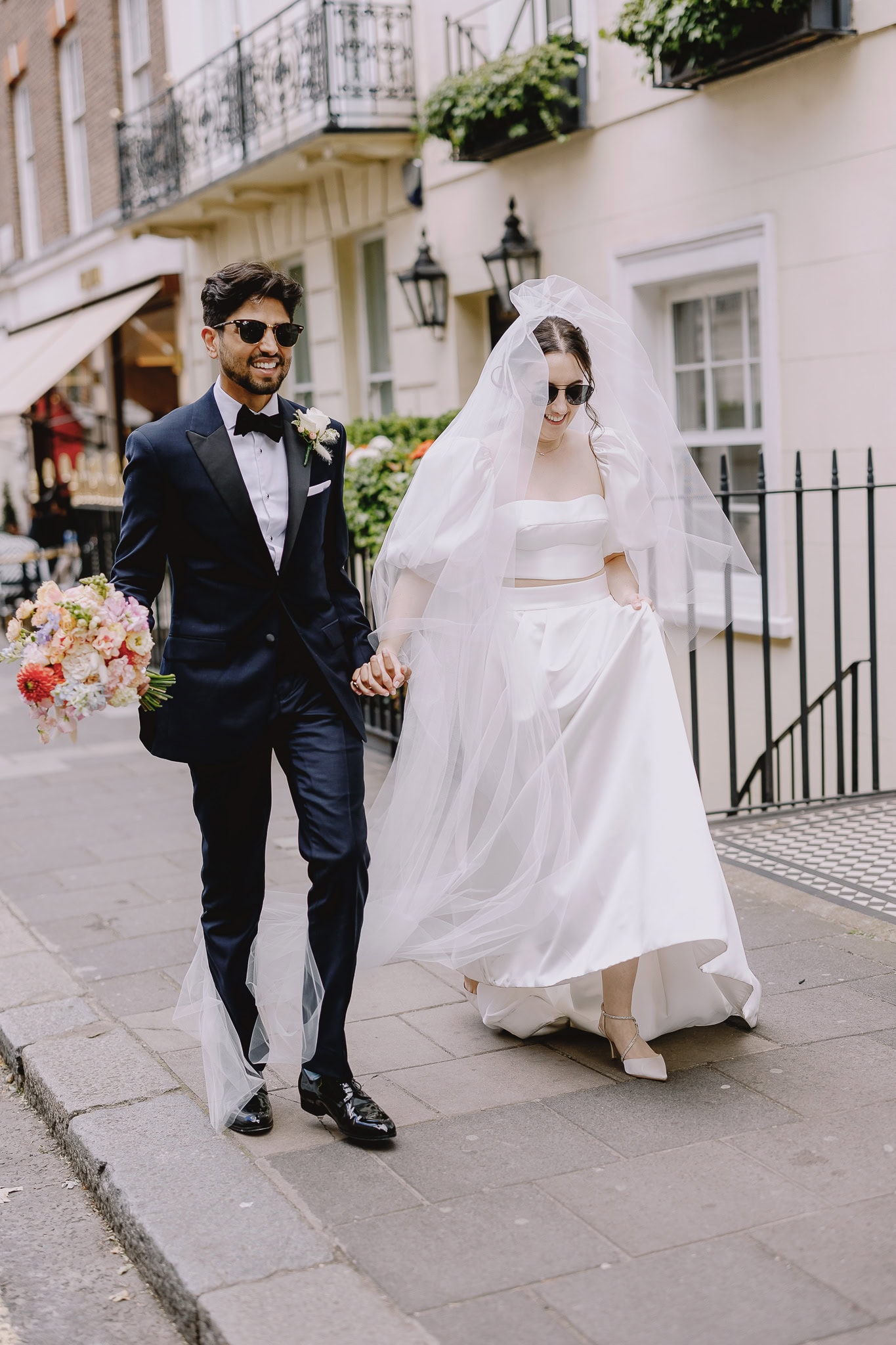 Stylish couple during editorial wedding photography, walking hand-in-hand on city street.