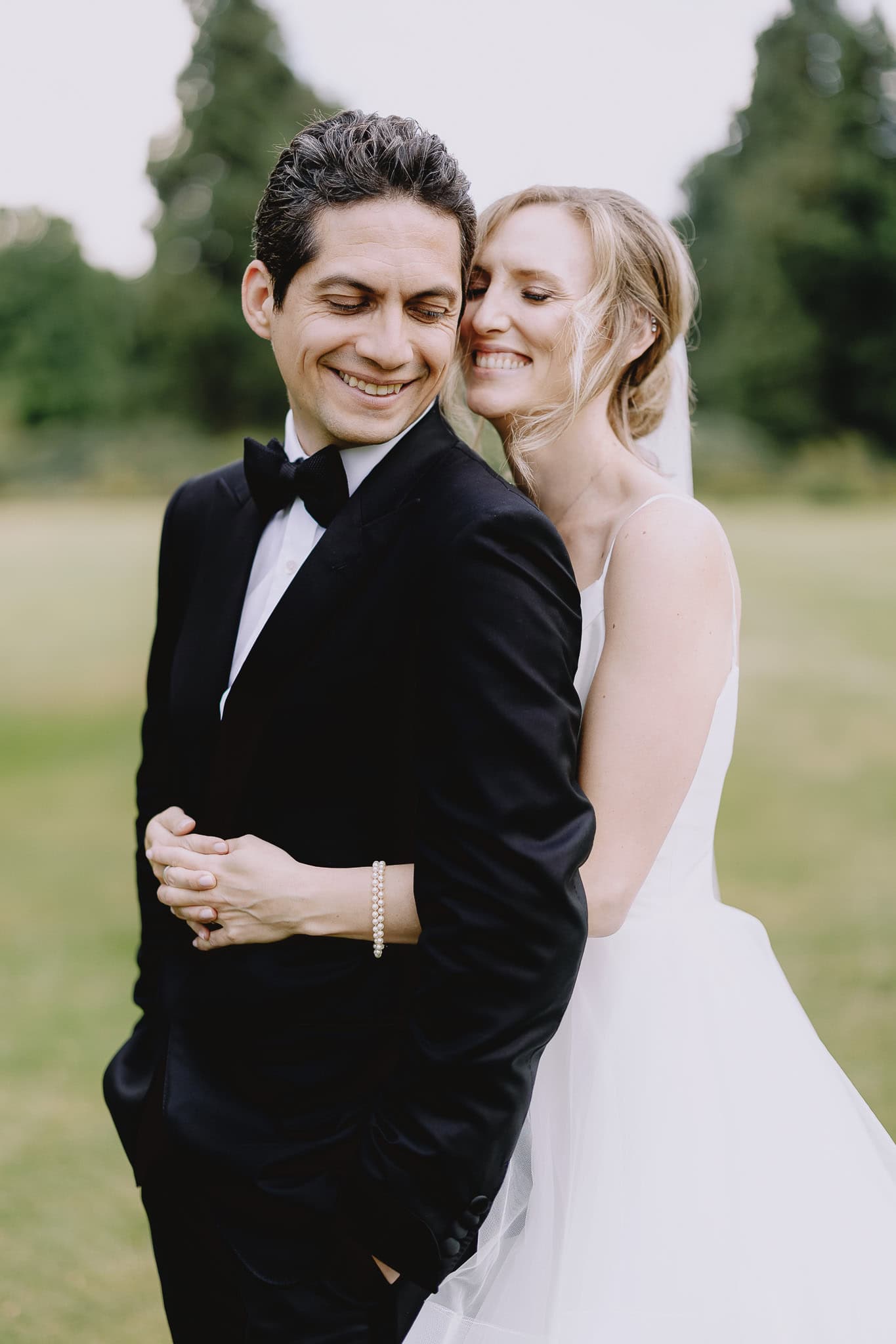 Bride embraces groom in black tuxedo, smiling during editorial wedding photography session.