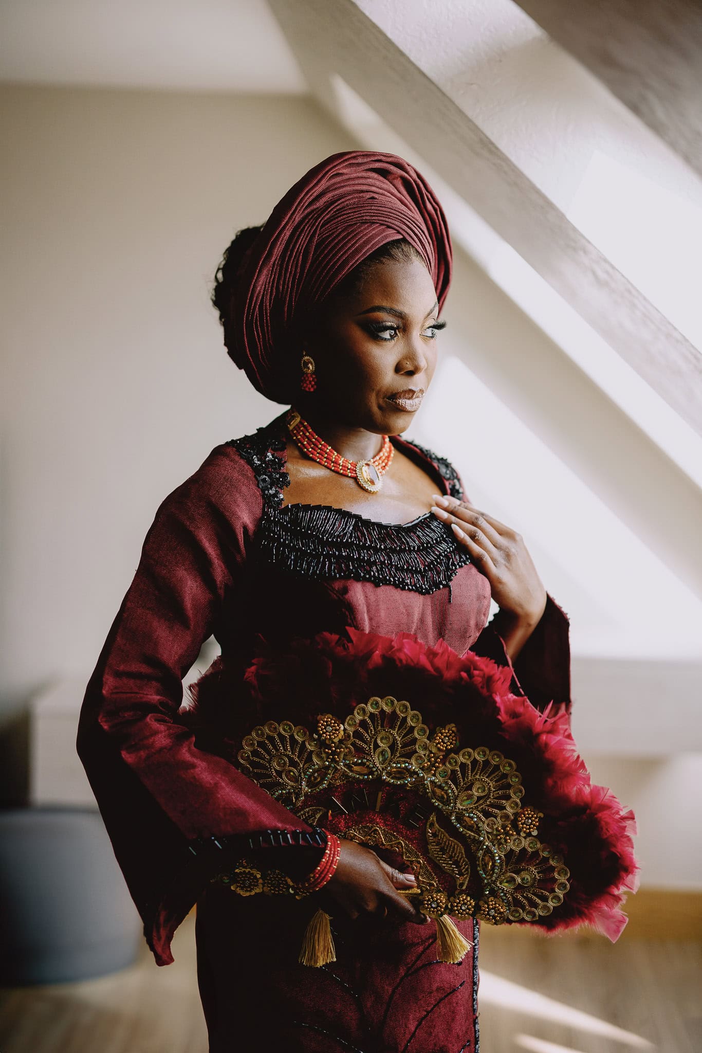 Woman in traditional burgundy Nigerian wedding attire with headwrap and beaded jewelry.