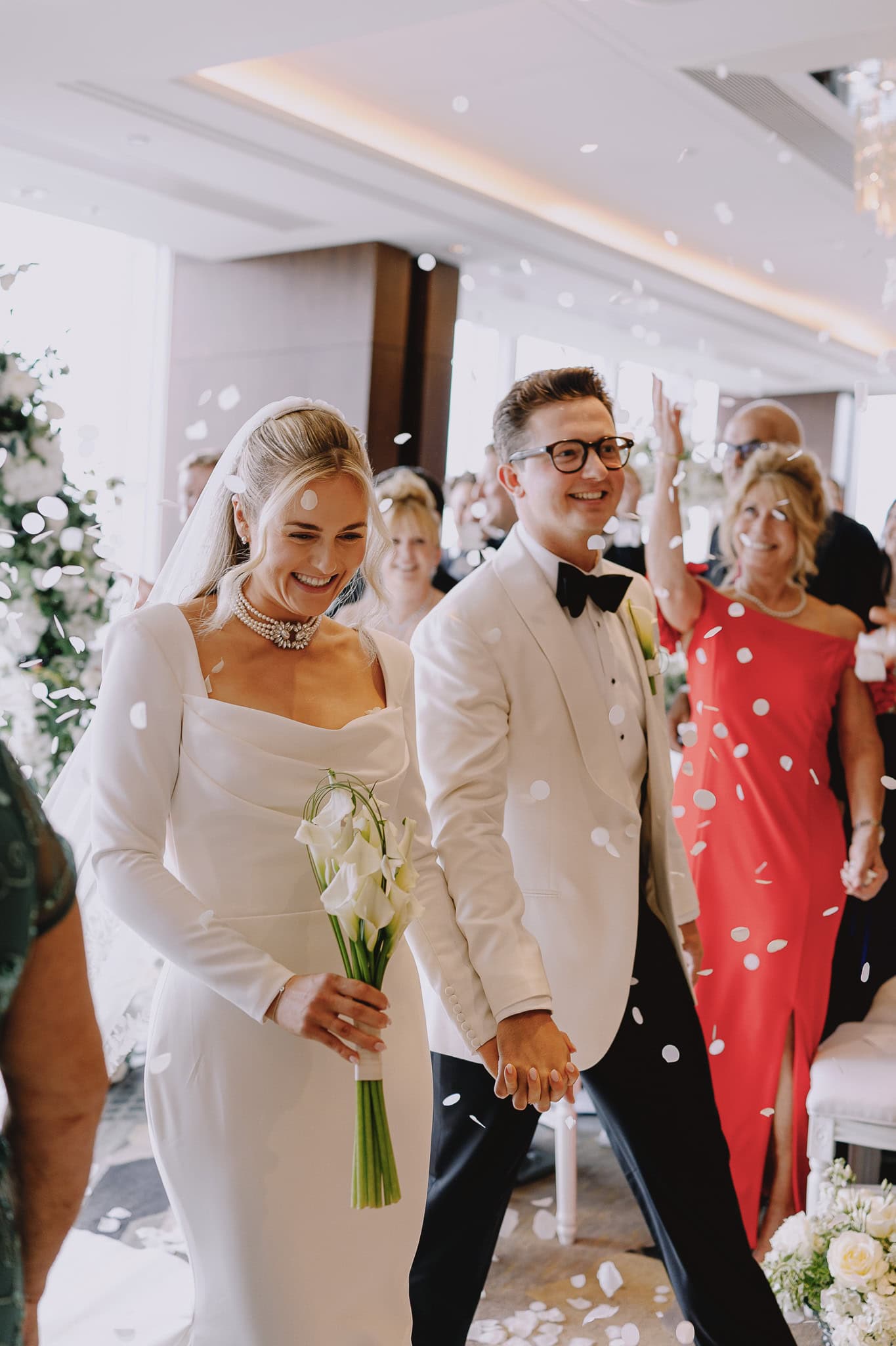Newlyweds walk under confetti, editorial wedding photography with bride in white dress and groom in tuxedo.