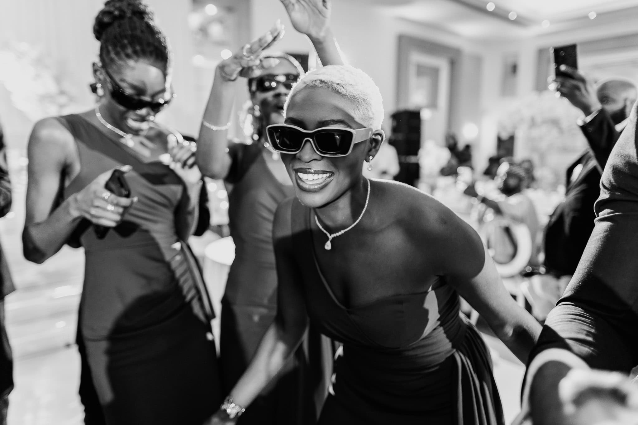 Joyful women dancing at a party, wearing sunglasses and elegant dresses.