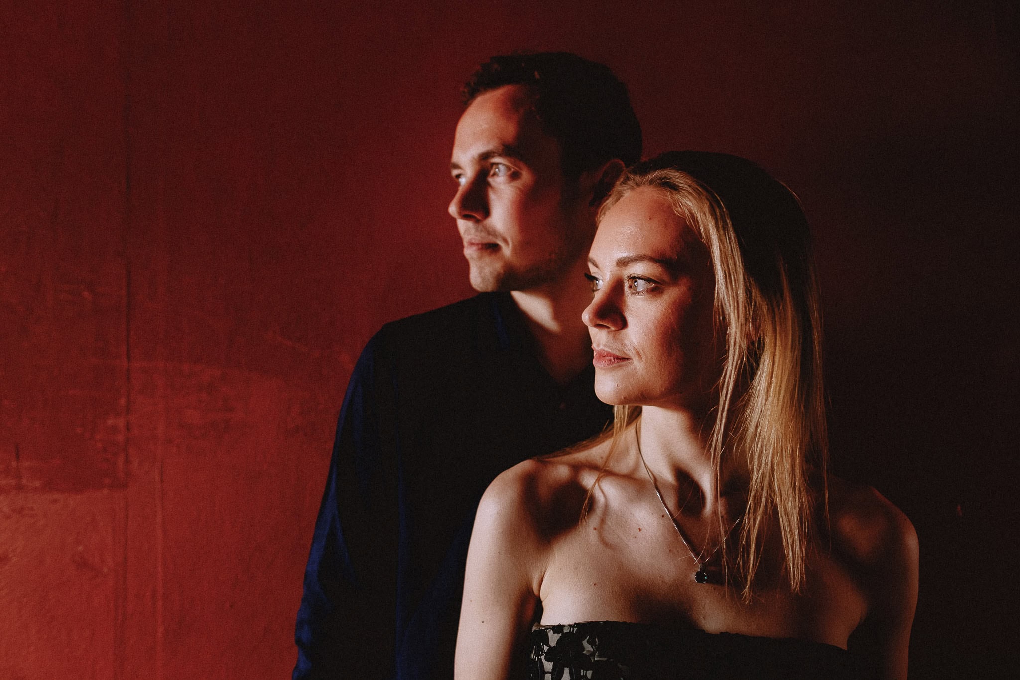 Elegant couple portrait against a red wall, part of a wedding photography portfolio.
