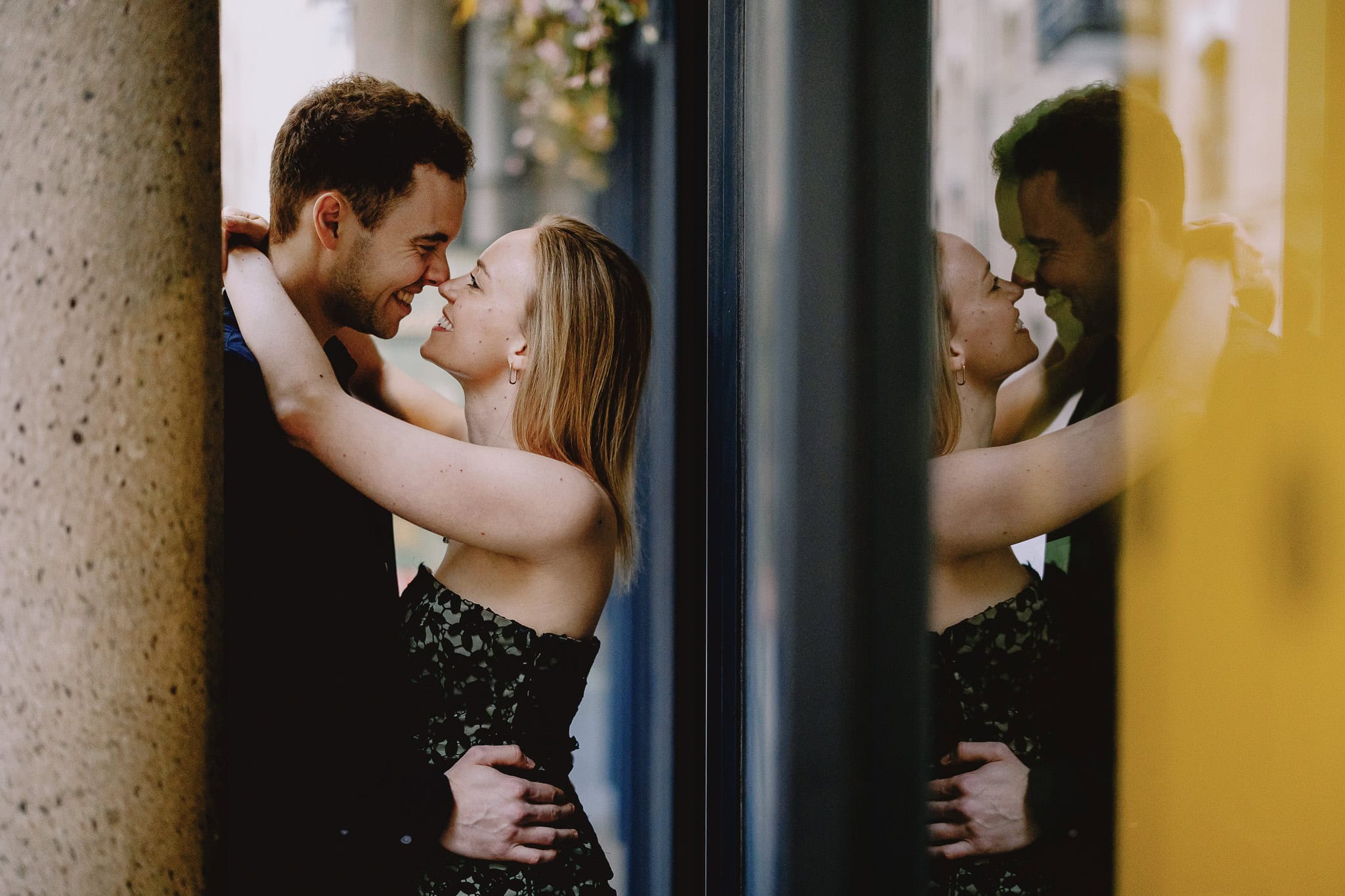 Couple embracing and smiling, reflected in a window. Romantic moment, love, and affection captured in a city setting.