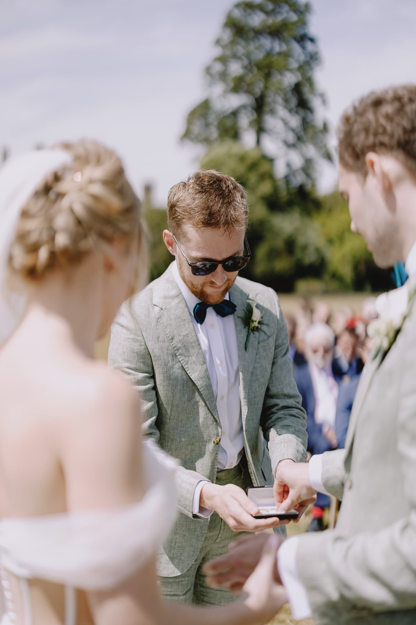 Groom's man hands wedding rings to the groom during outdoor ceremony.