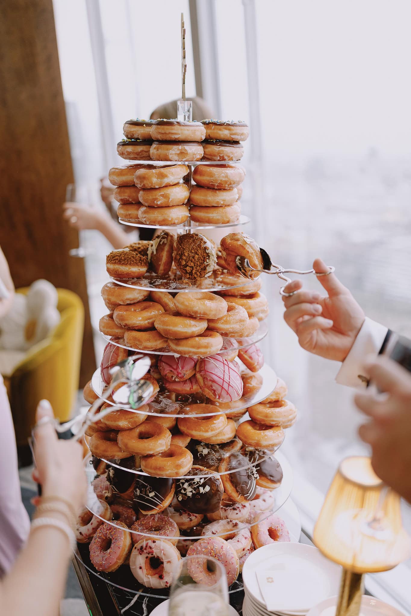 Donut tower at wedding reception; glazed, chocolate, and pink donuts on display.