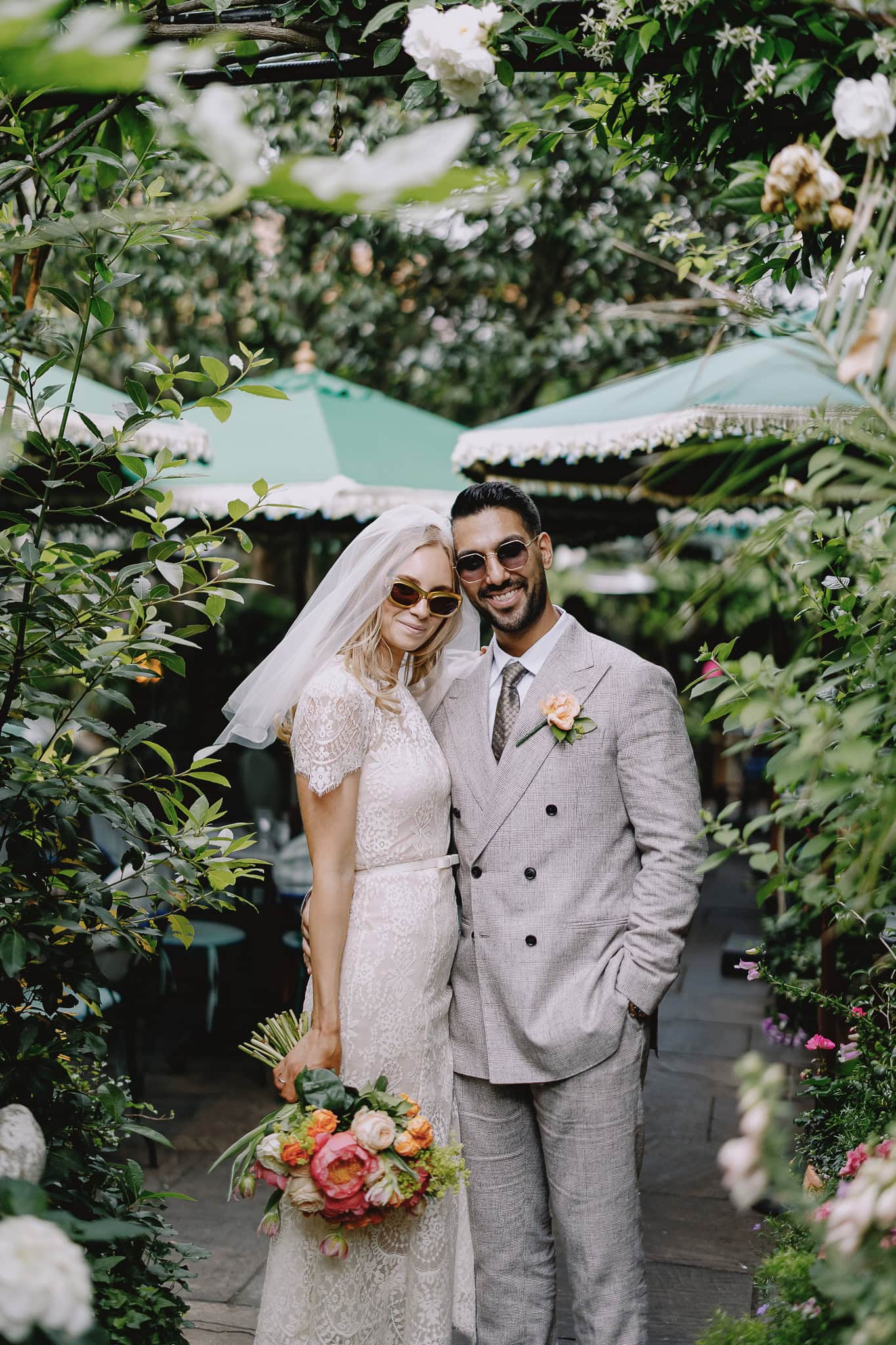 Stylish couple in wedding attire surrounded by lush greenery.