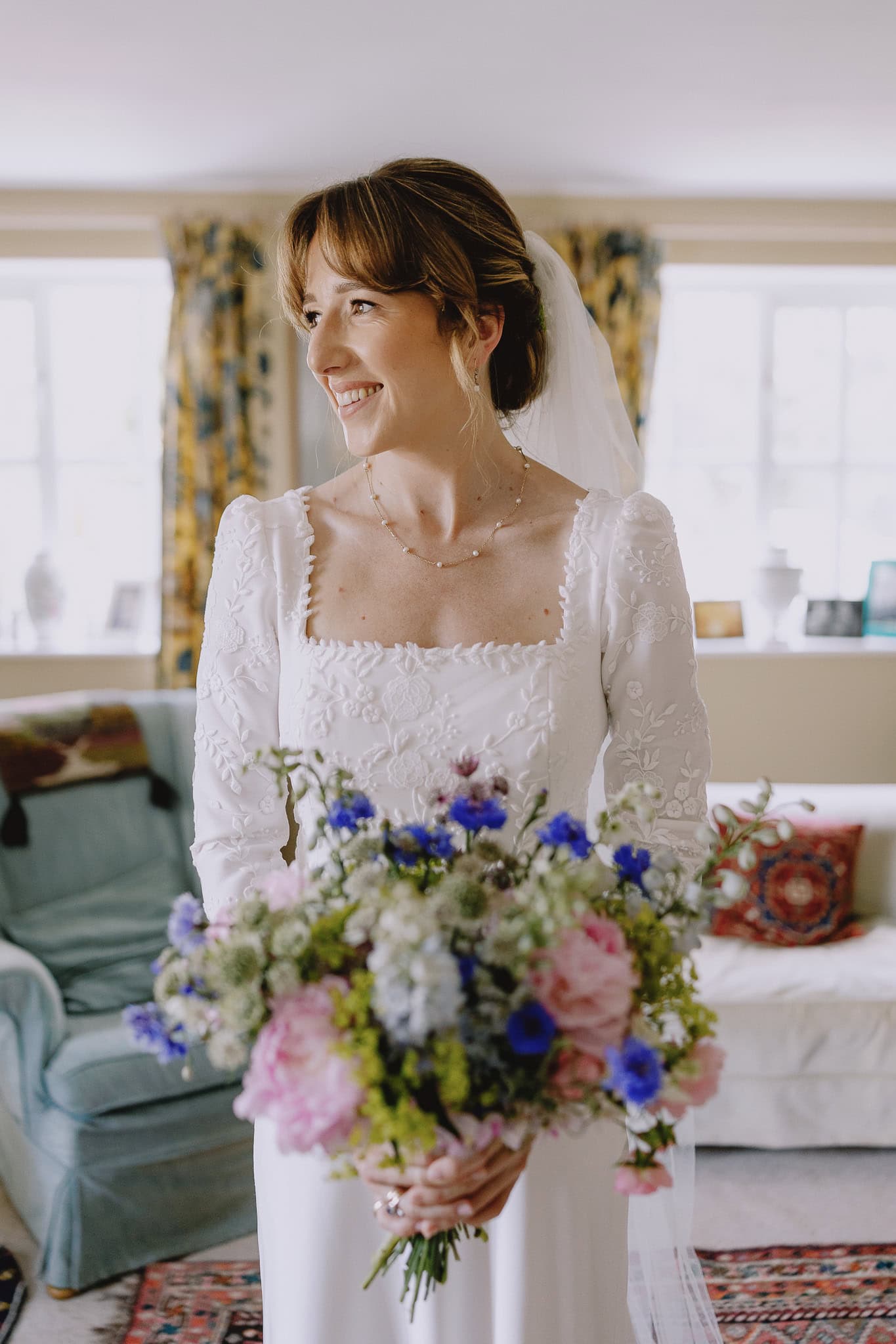 Smiling bride in white dress with floral bouquet and veil.