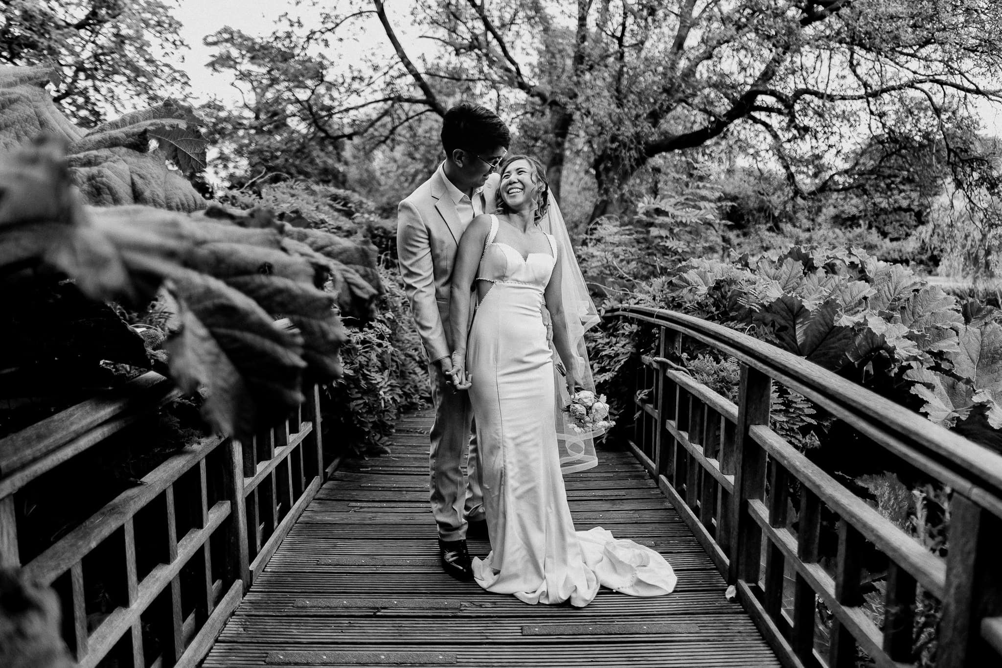 Happy bride and groom on a wooden bridge in a garden, wedding day portrait.