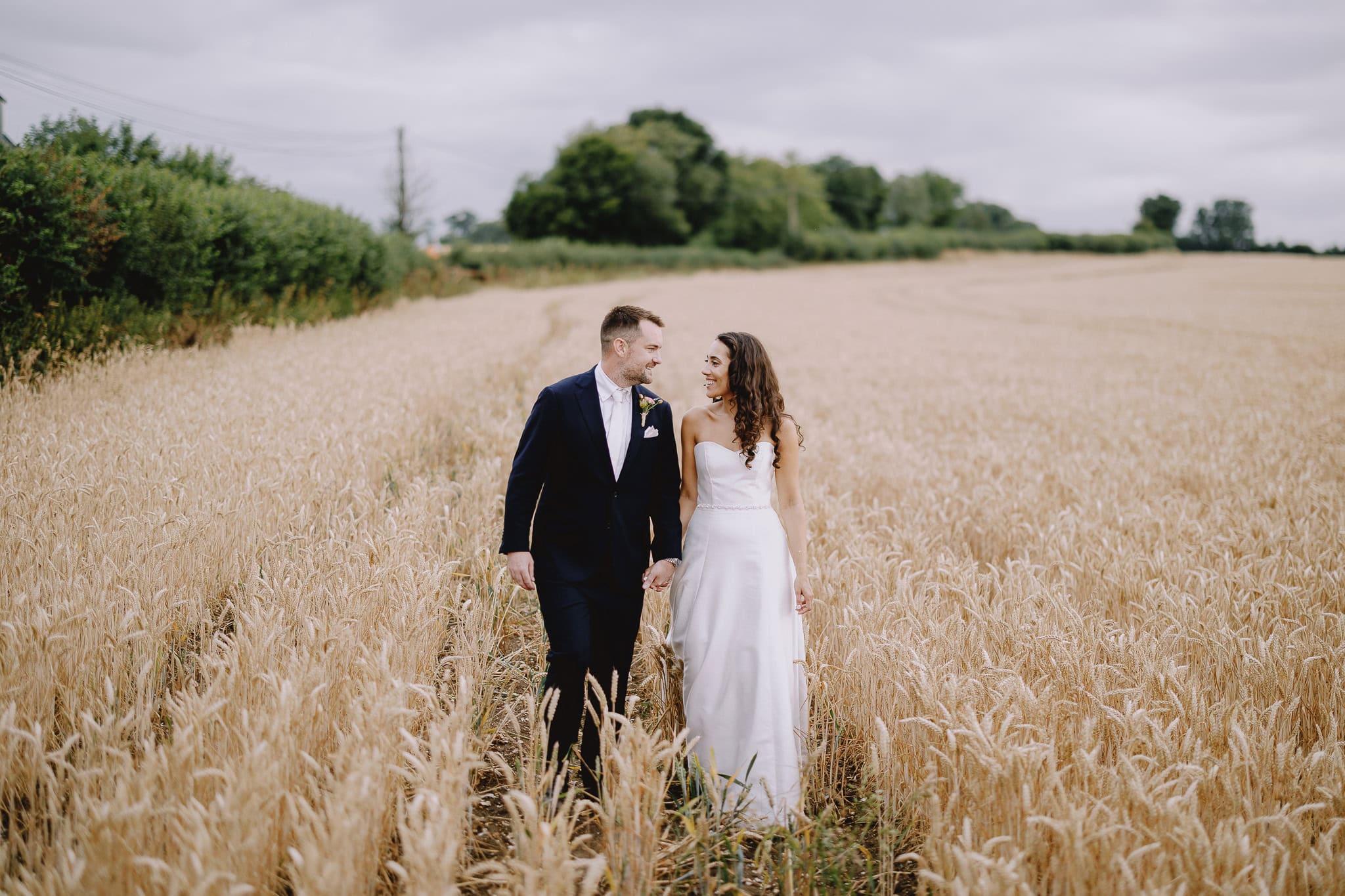 Wedding photography portfolio: Bride and groom walking through wheat field.