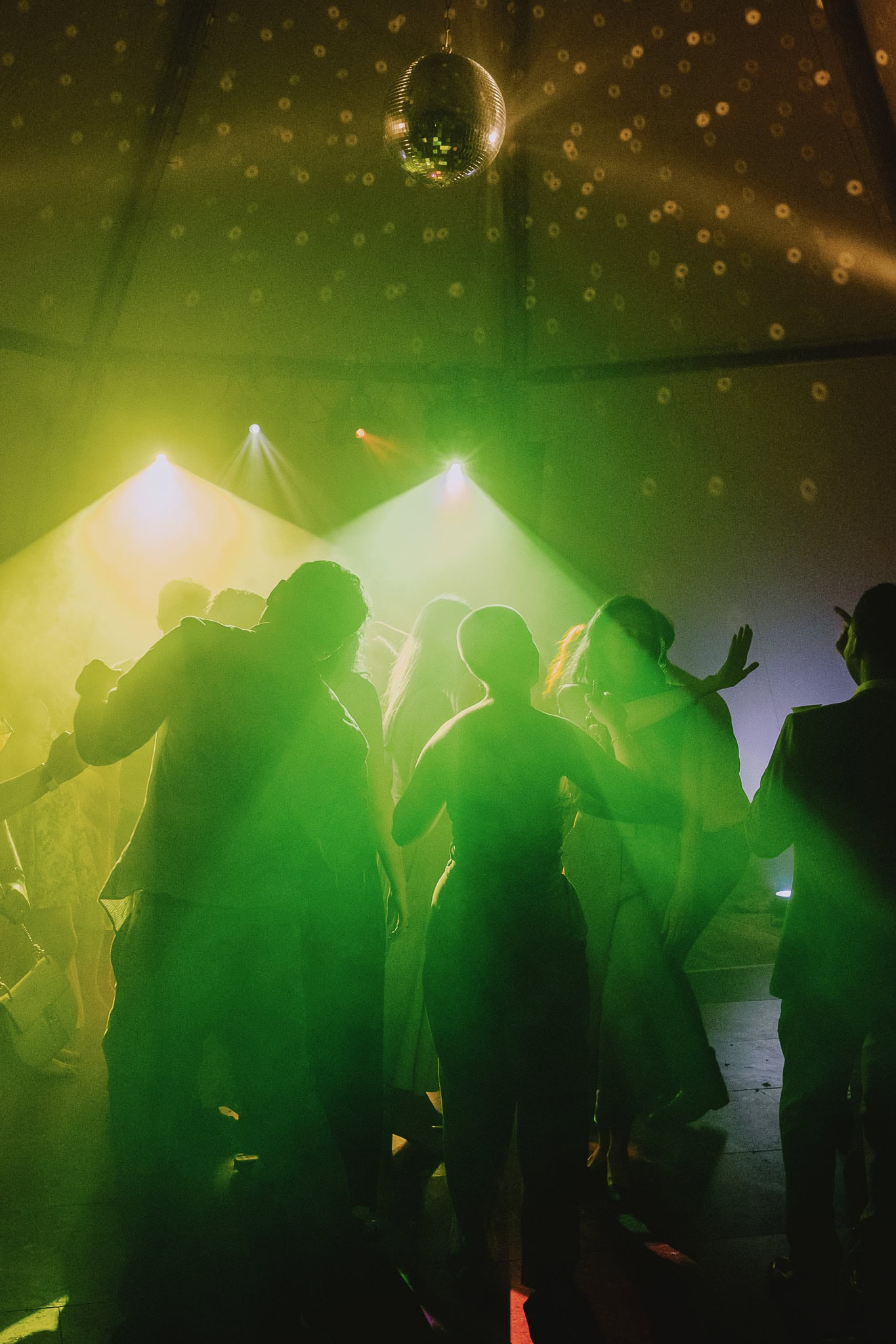 People dancing under a disco ball and green lights at a party.