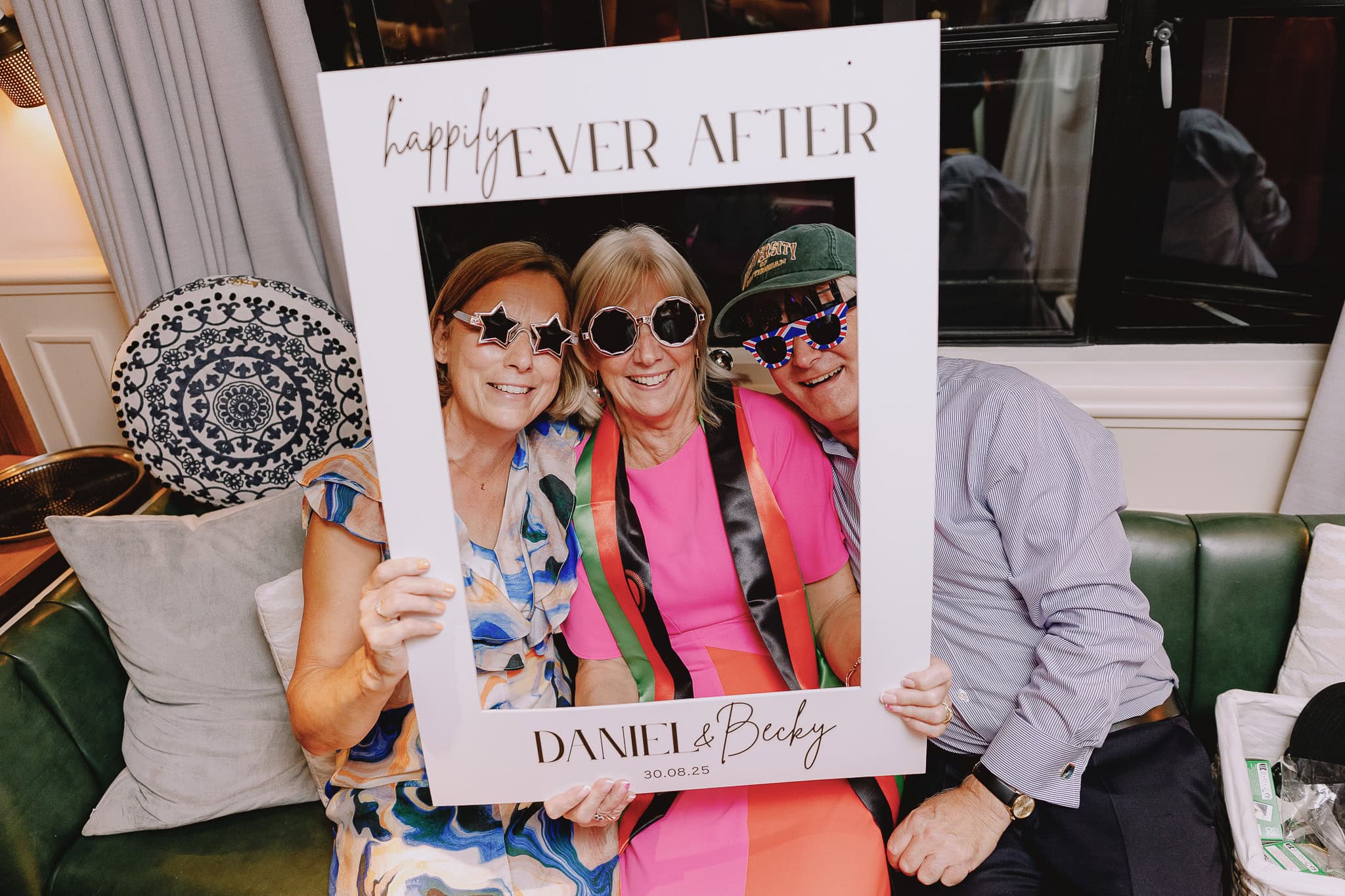 Wedding guests pose with "Happily Ever After" frame at Daniel & Becky's wedding. Silly glasses, fun celebration.