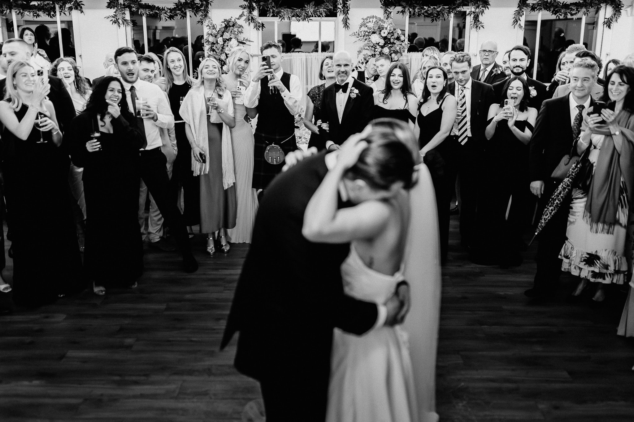 Bride and groom share a first dance, surrounded by wedding guests.