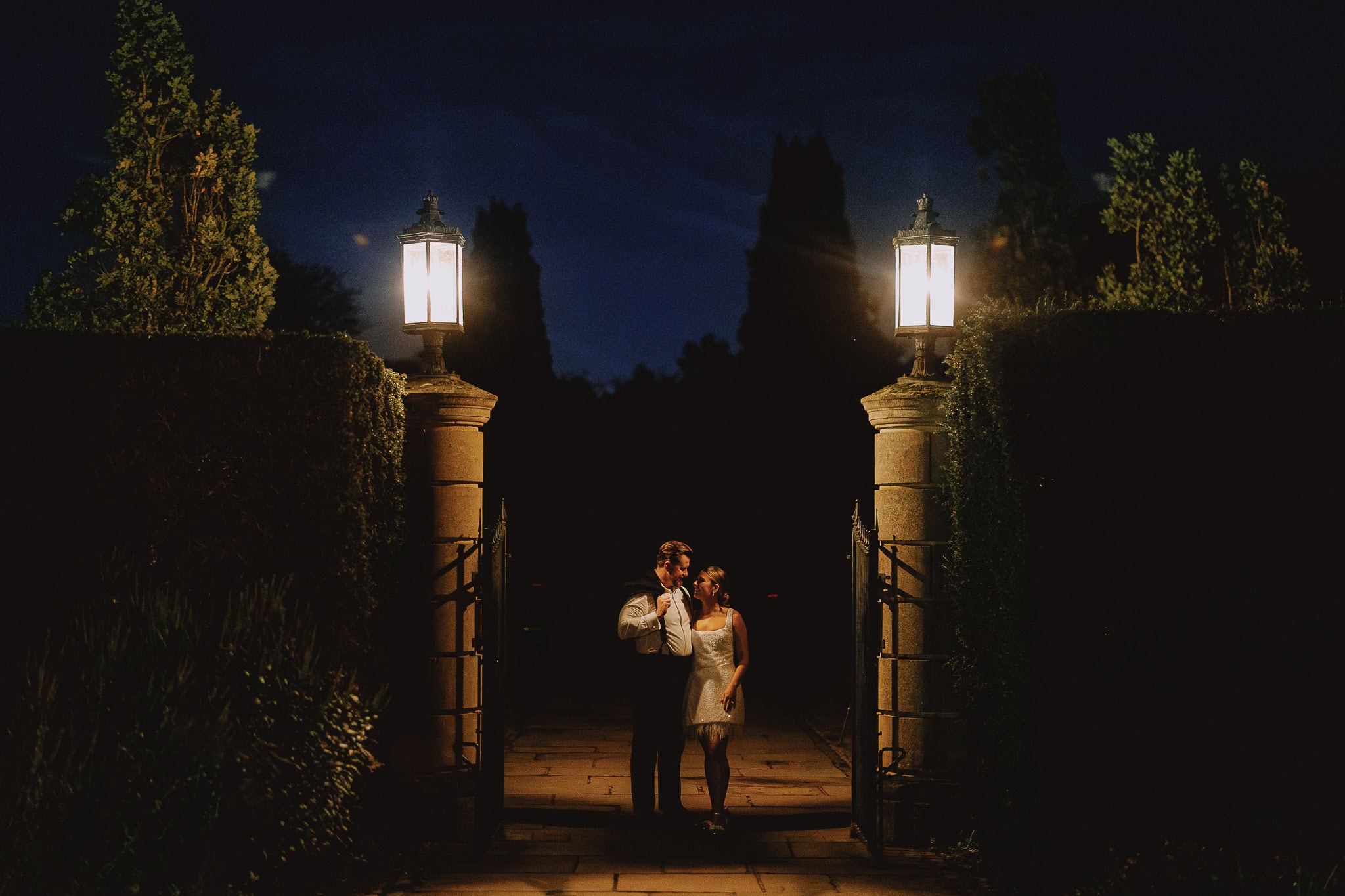 Night wedding photography portfolio: Couple by illuminated gate.
