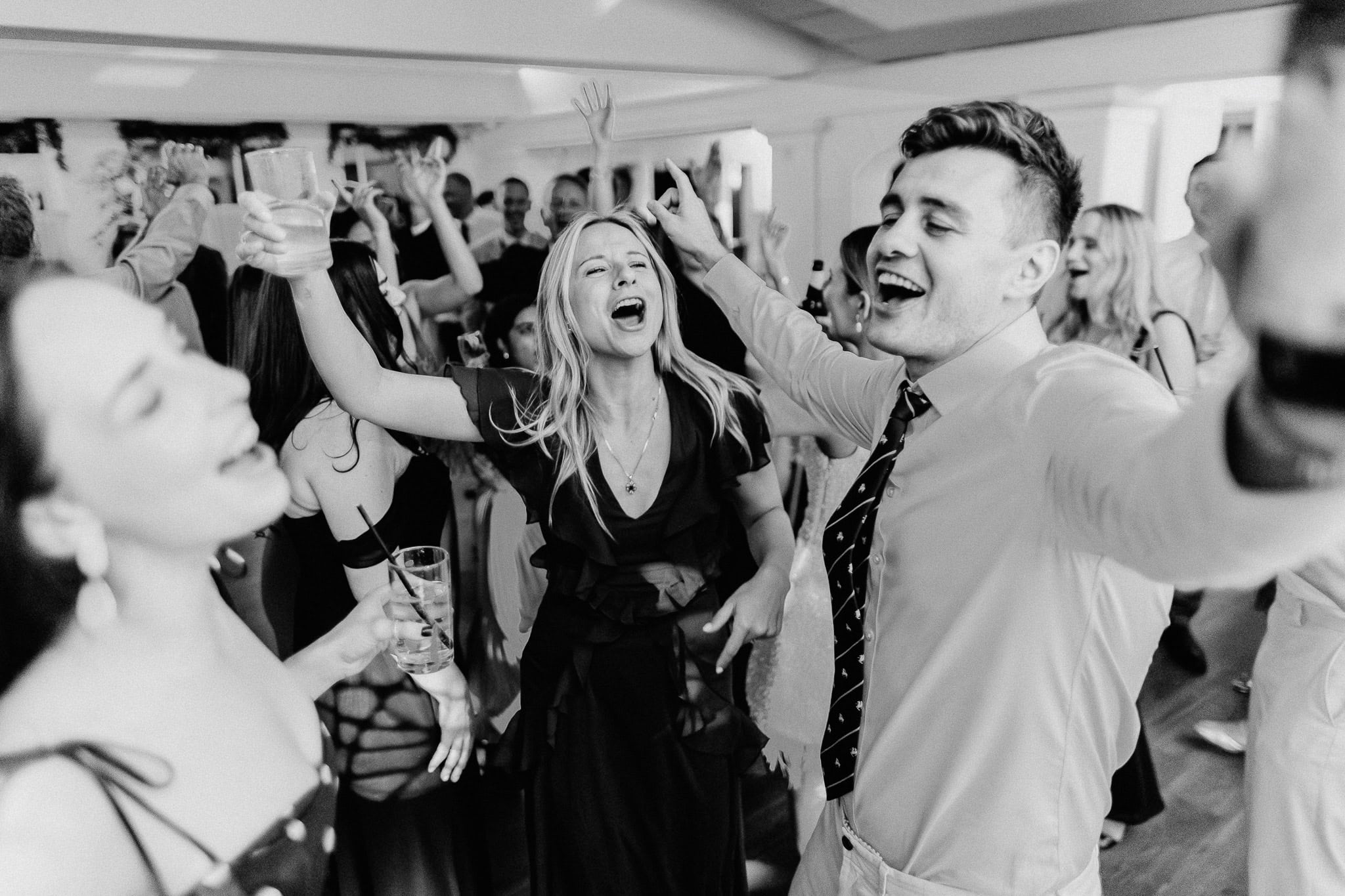 Wedding guests joyfully dancing at a reception, arms raised. Wedding Photography Portfolio.