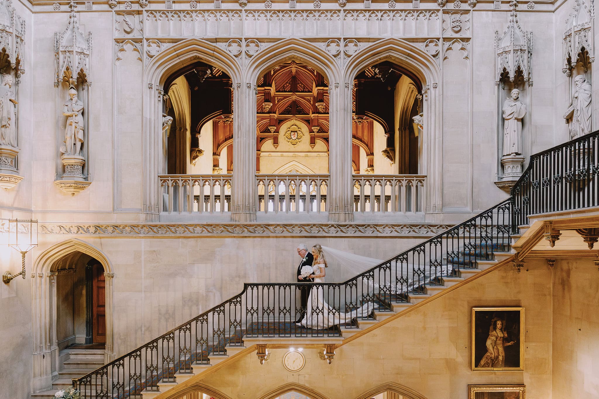Bride and father walking down grand staircase at wedding venue.