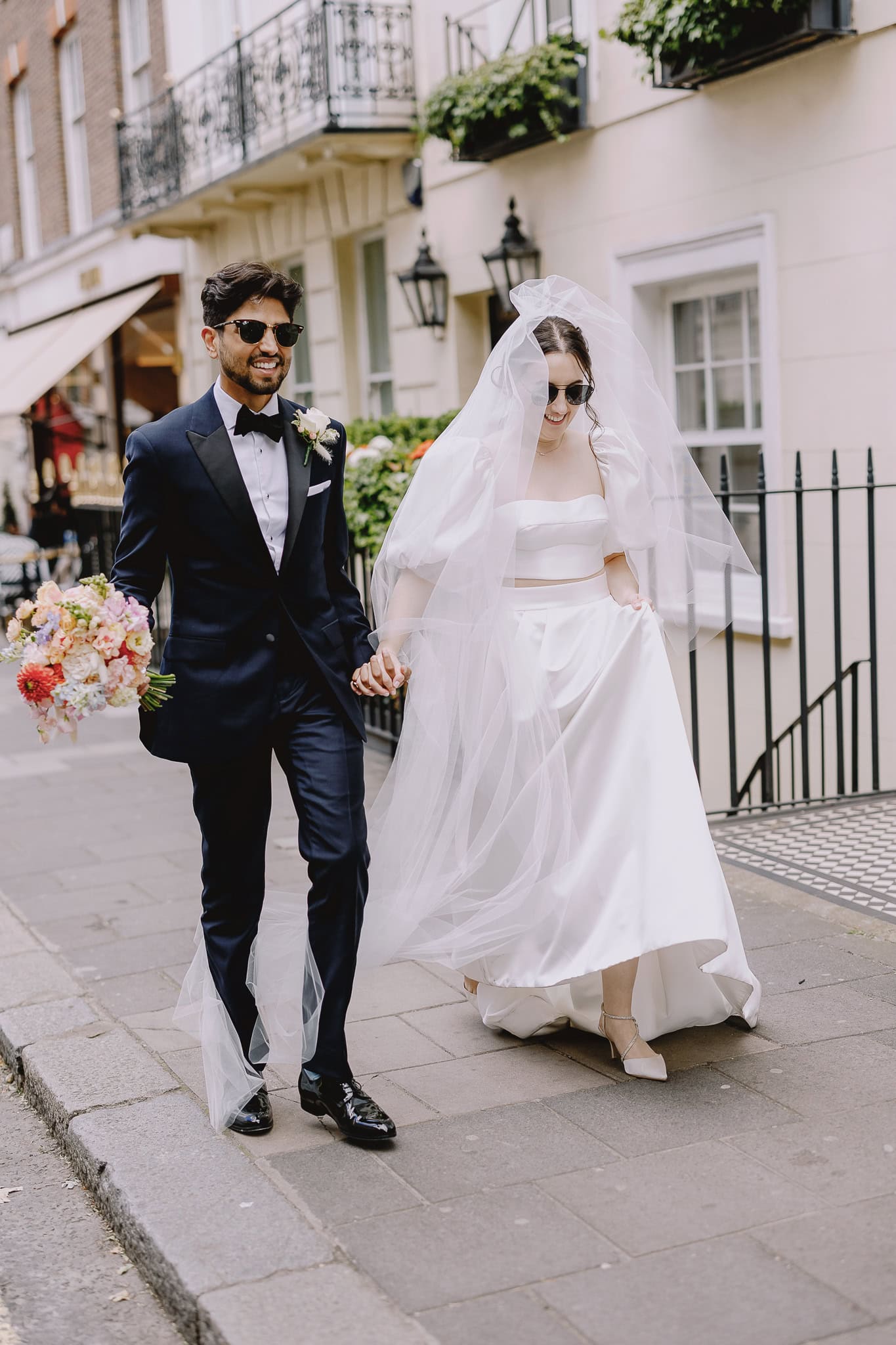 Stylish couple wearing sunglasses, walking on their wedding day.