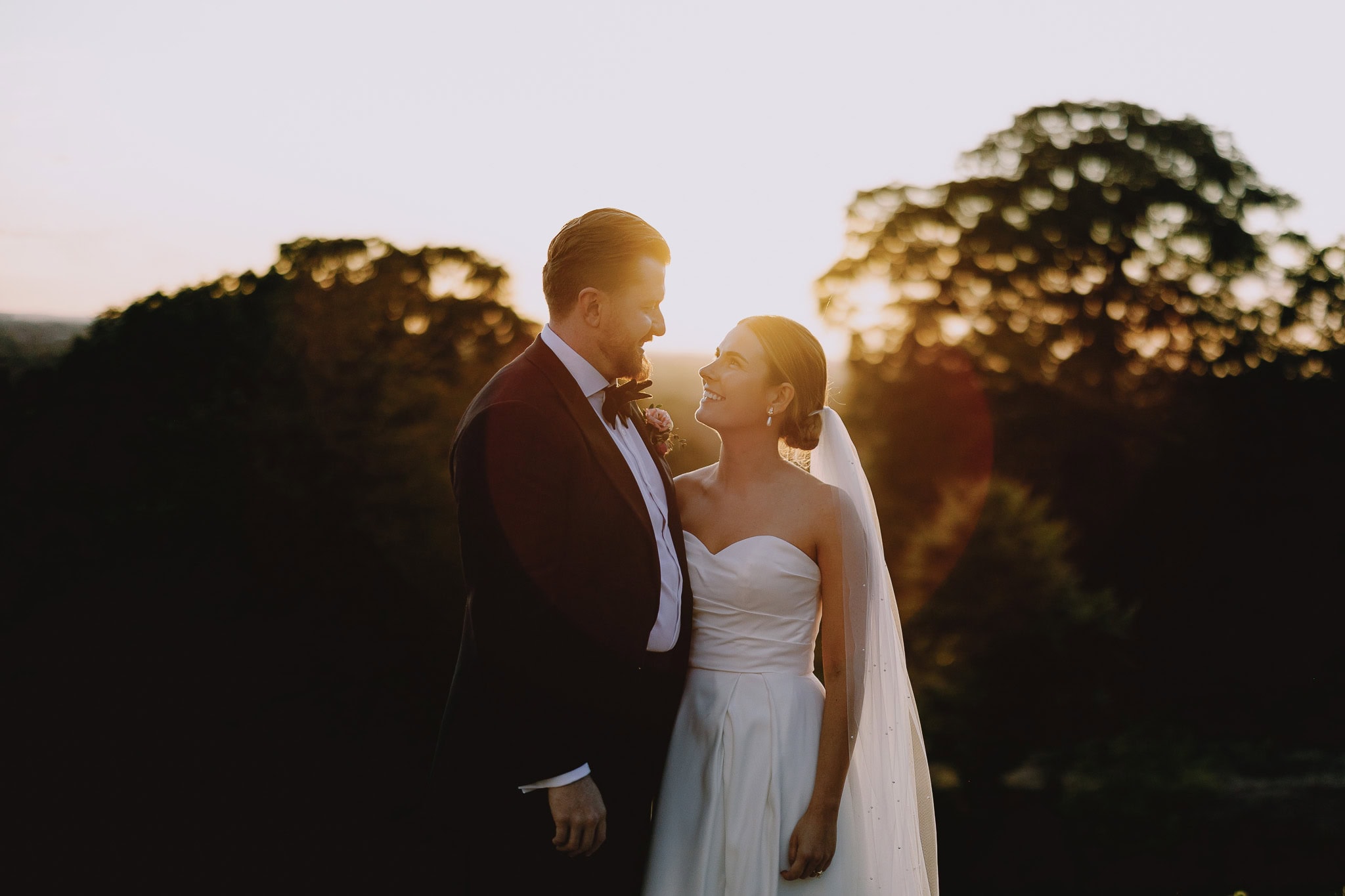 Bride and groom at a countryside wedding, bathed in golden sunset light.