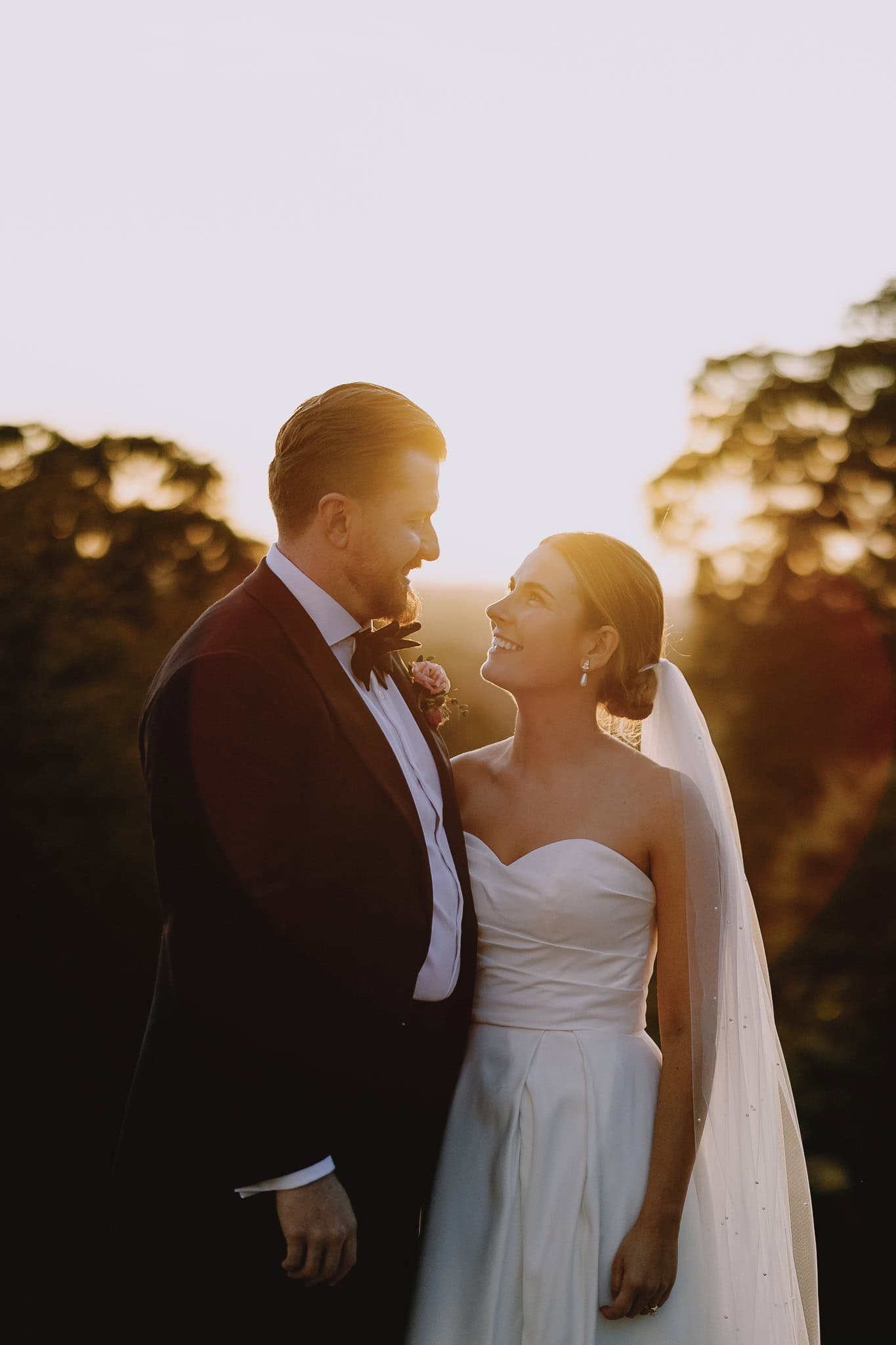 Bride and groom in formal wear gaze at each other during golden hour at their wedding.