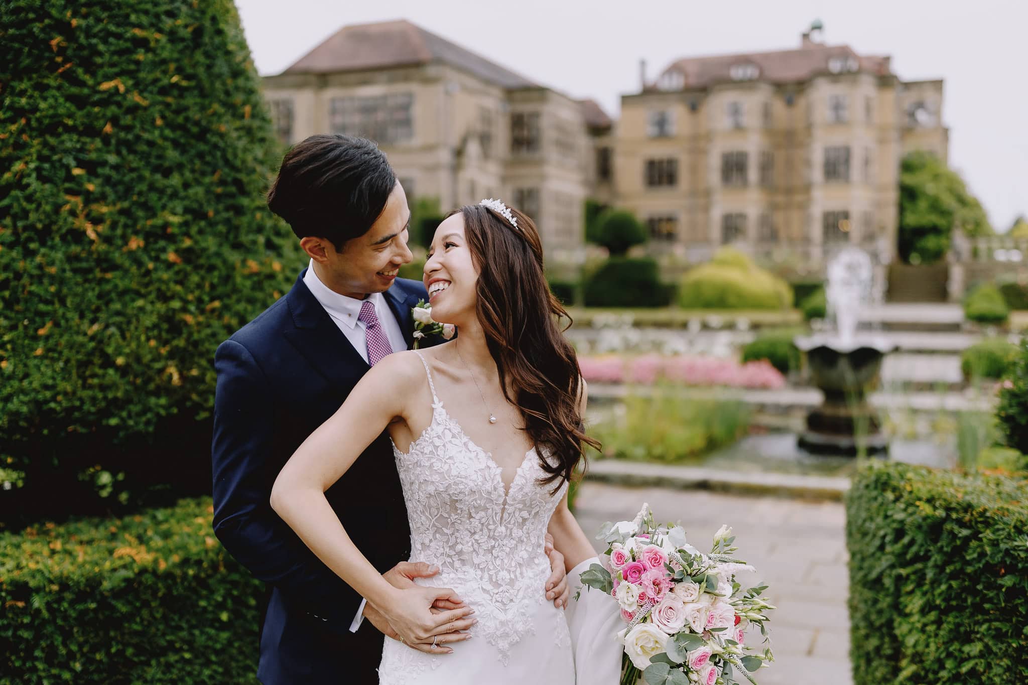 Fanhams Hall Wedding Photographer: Bride and groom smiling in front of a grand building and garden