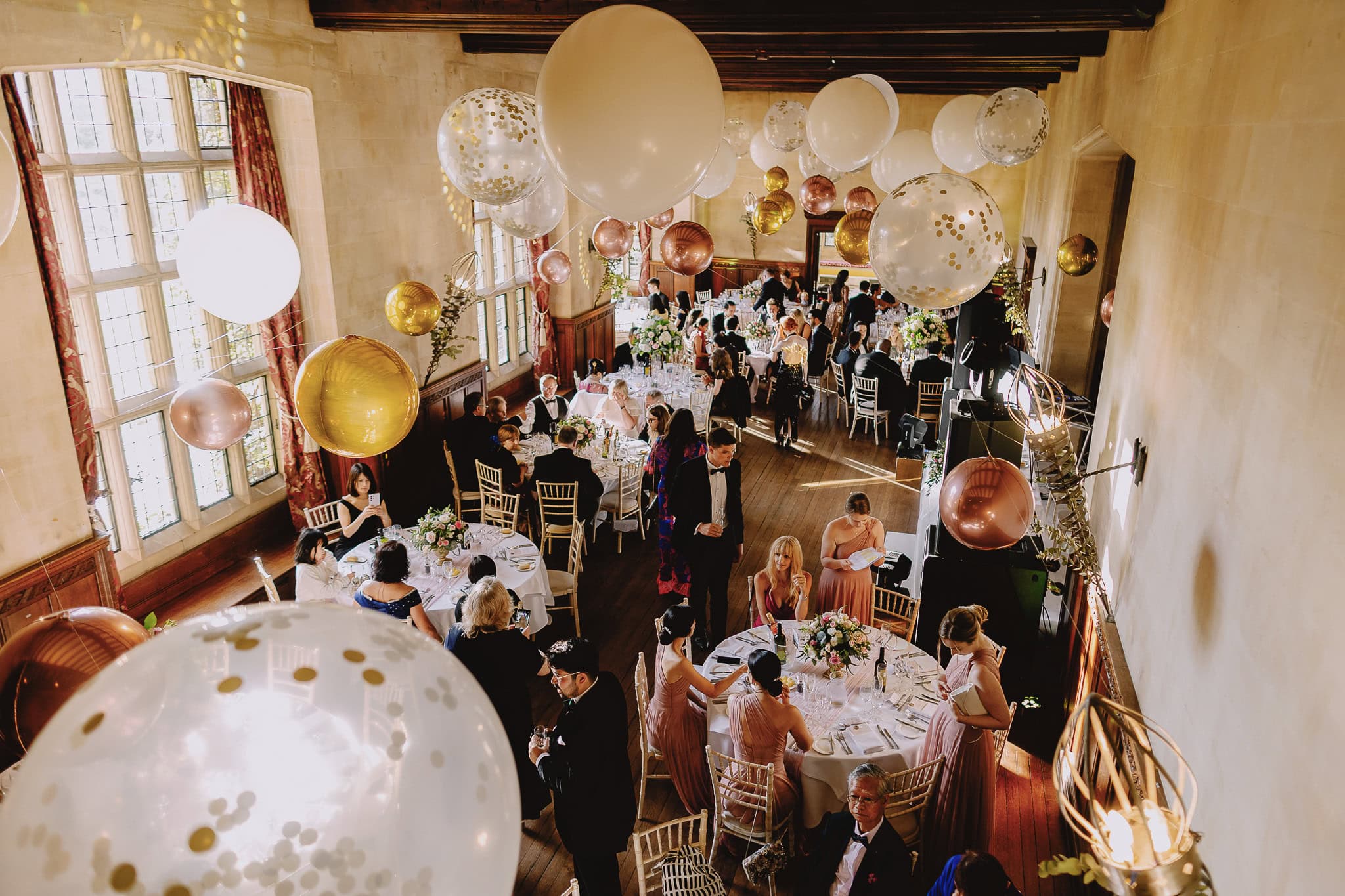 Wedding reception hall with round tables, balloons, and guests.