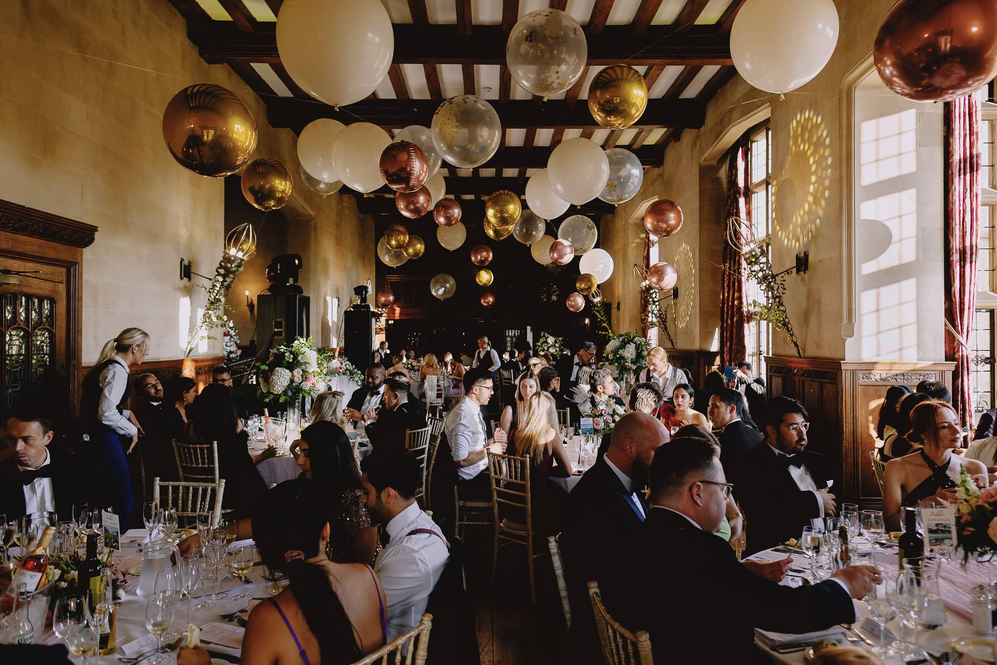 Elegant wedding reception with guests at tables under balloon decorations.