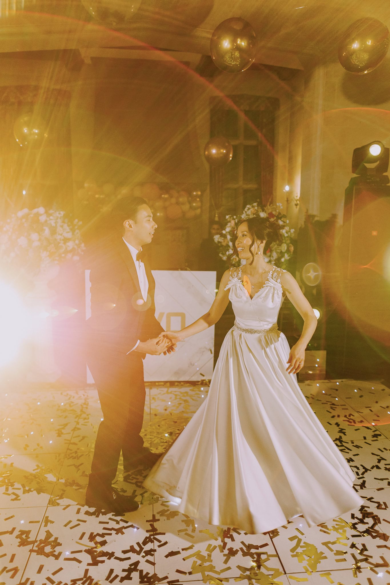 Bride and groom share their first dance under golden lights and confetti at their wedding reception.