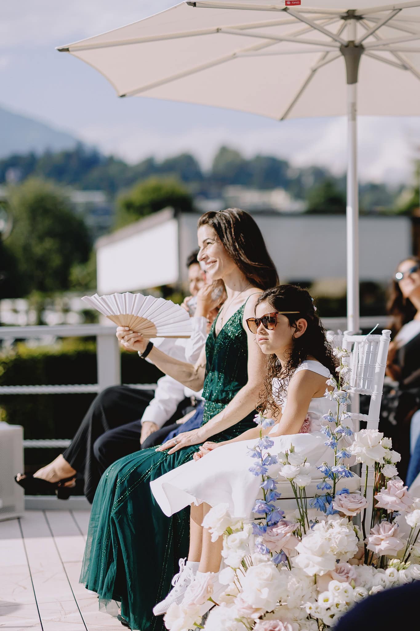 Wedding guest with fan and child at outdoor ceremony.
