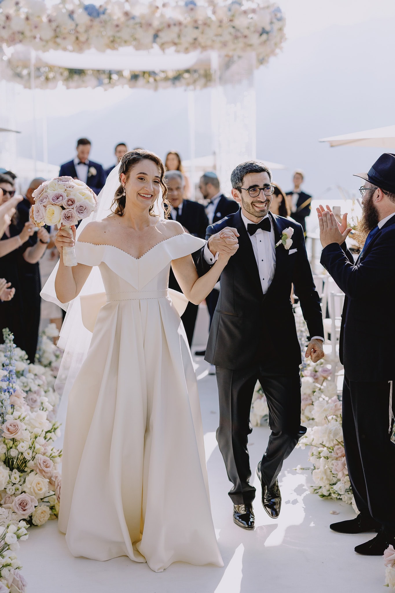 Joyful bride and groom exiting chuppah after Jewish wedding ceremony.
