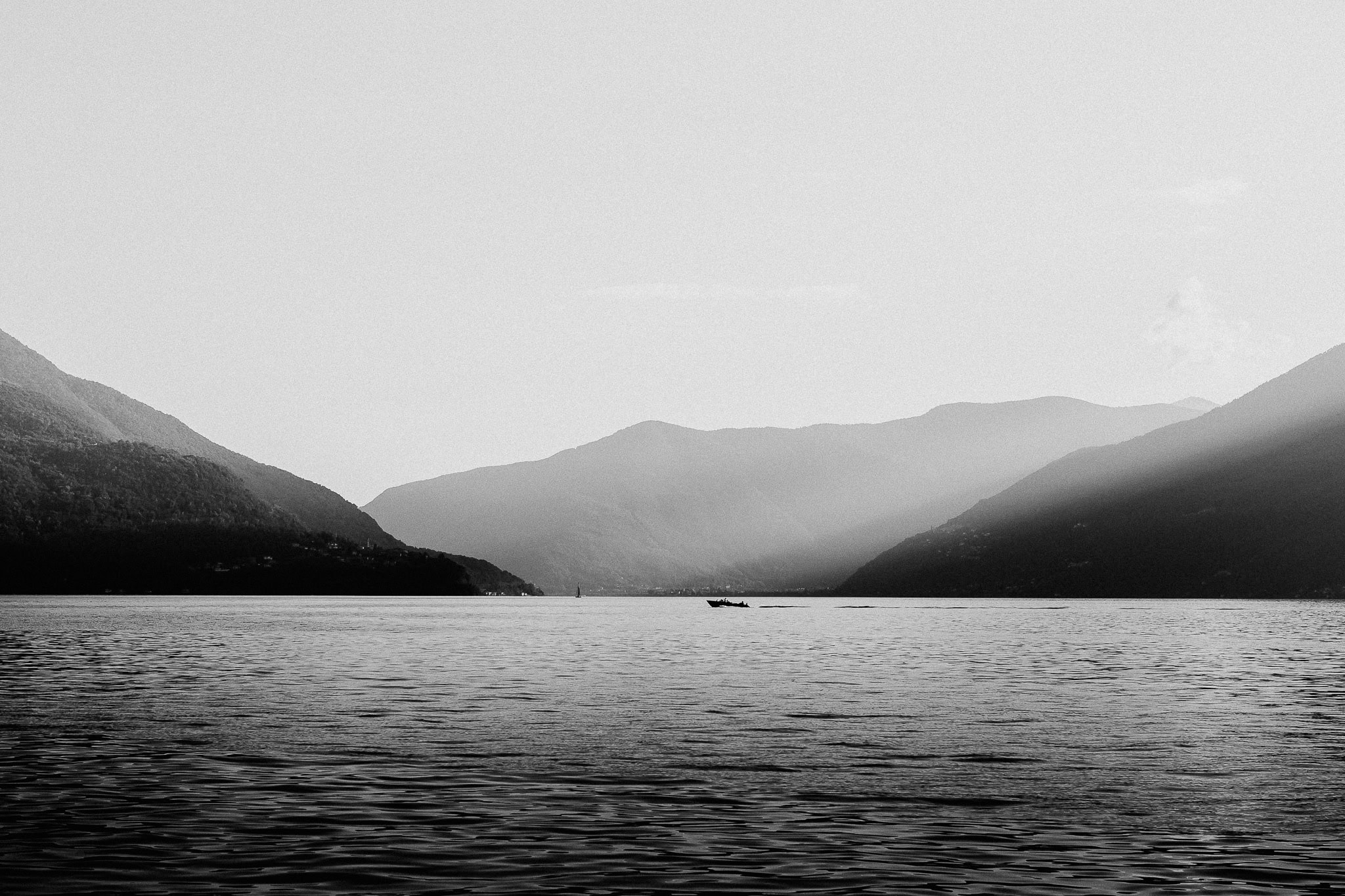 Boat on a calm lake surrounded by mountains in black and white
