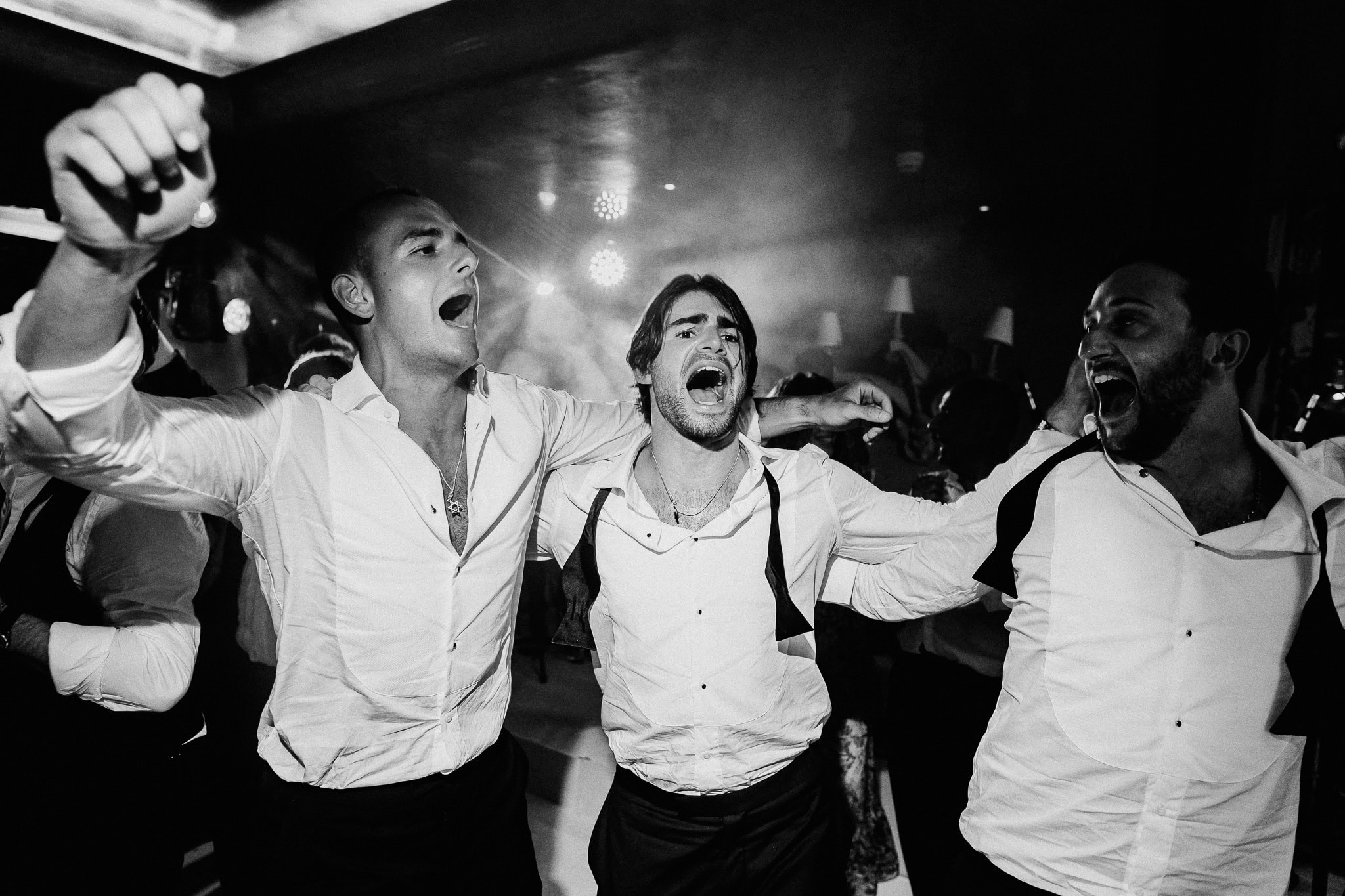 Groom and groomsmen joyfully dancing at wedding reception.