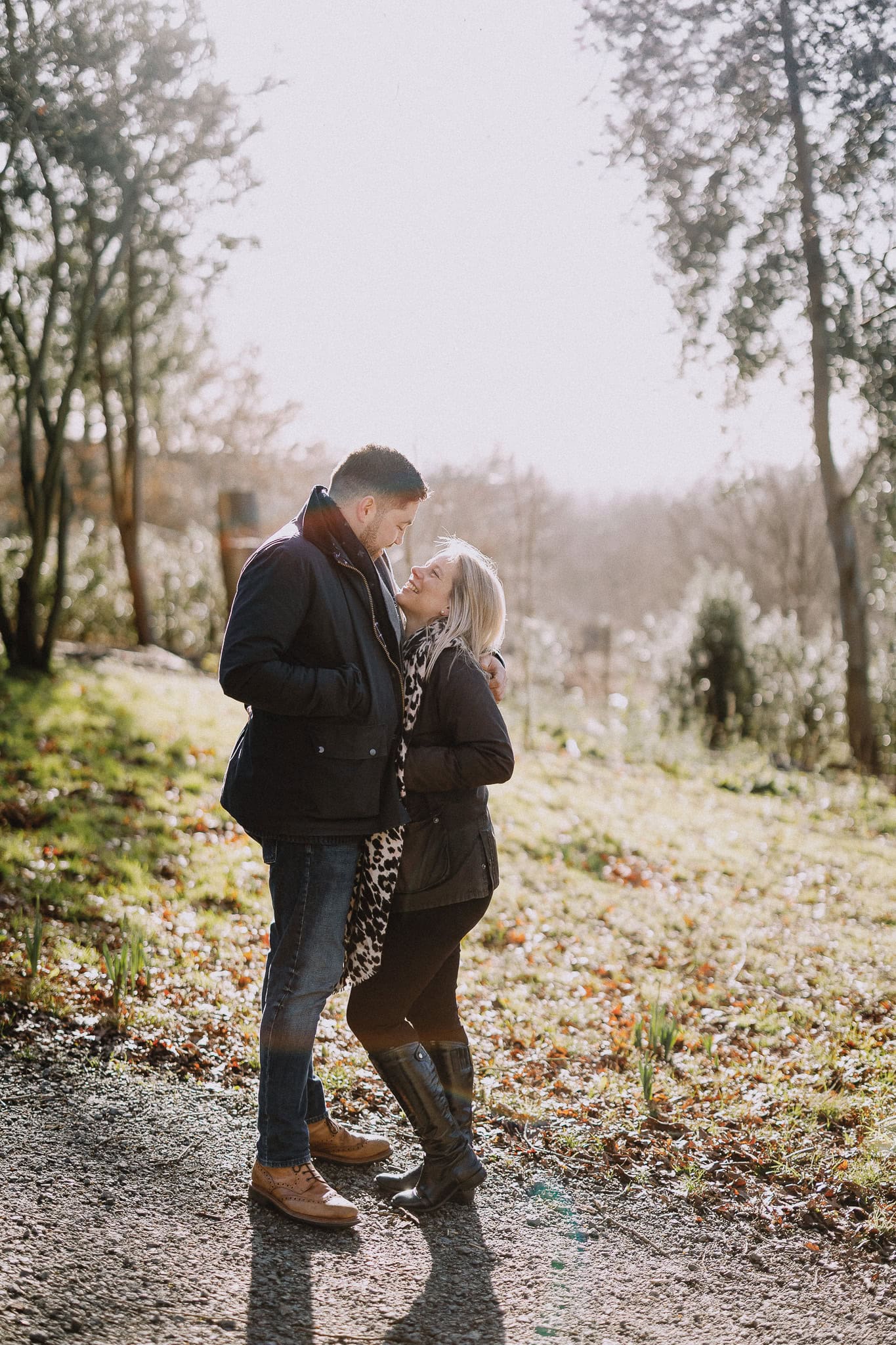 Couple embracing in a park, looking at each other with affection. Sunlight filters through the trees.