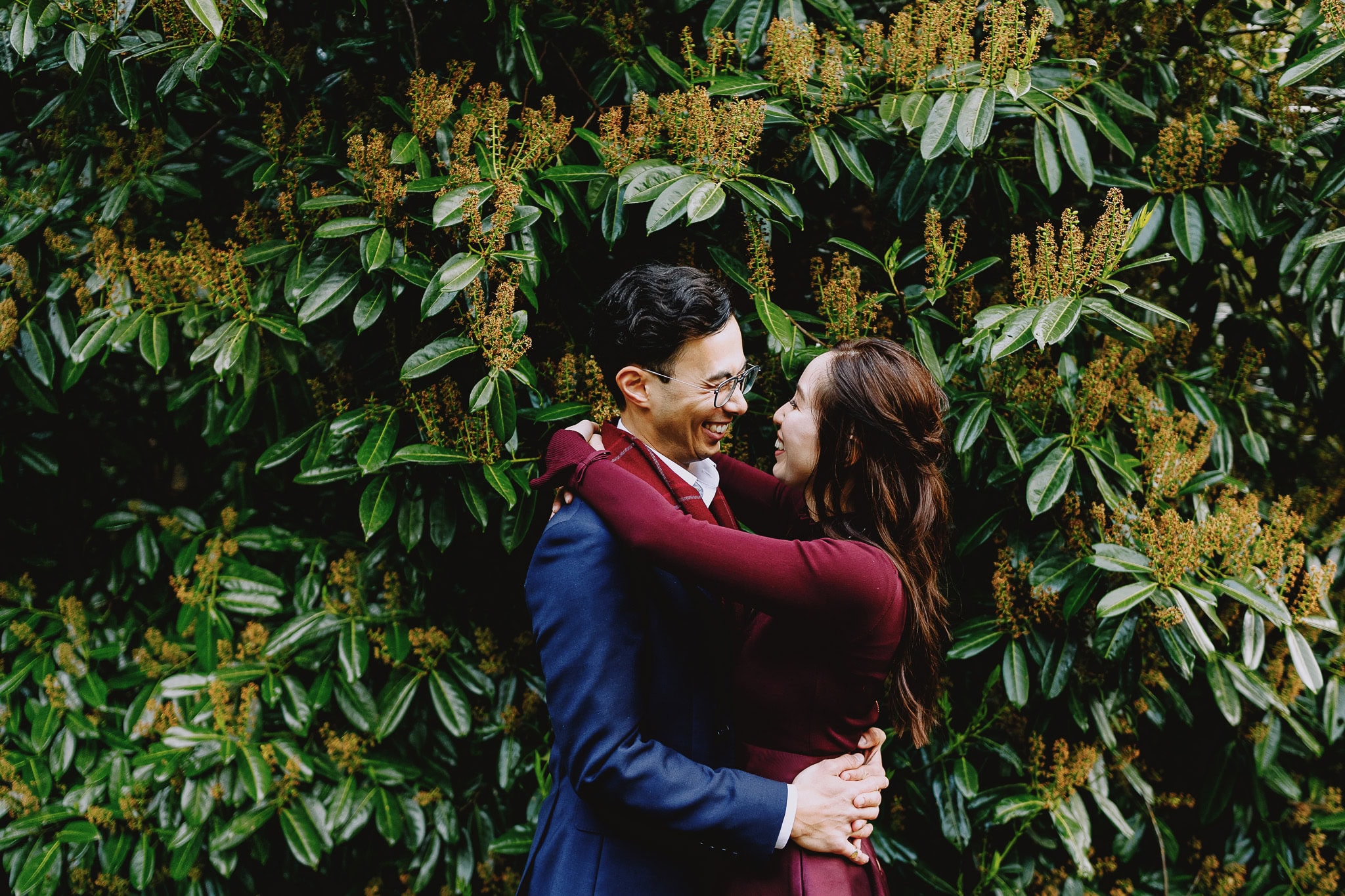 Happy couple embracing in front of lush green foliage.