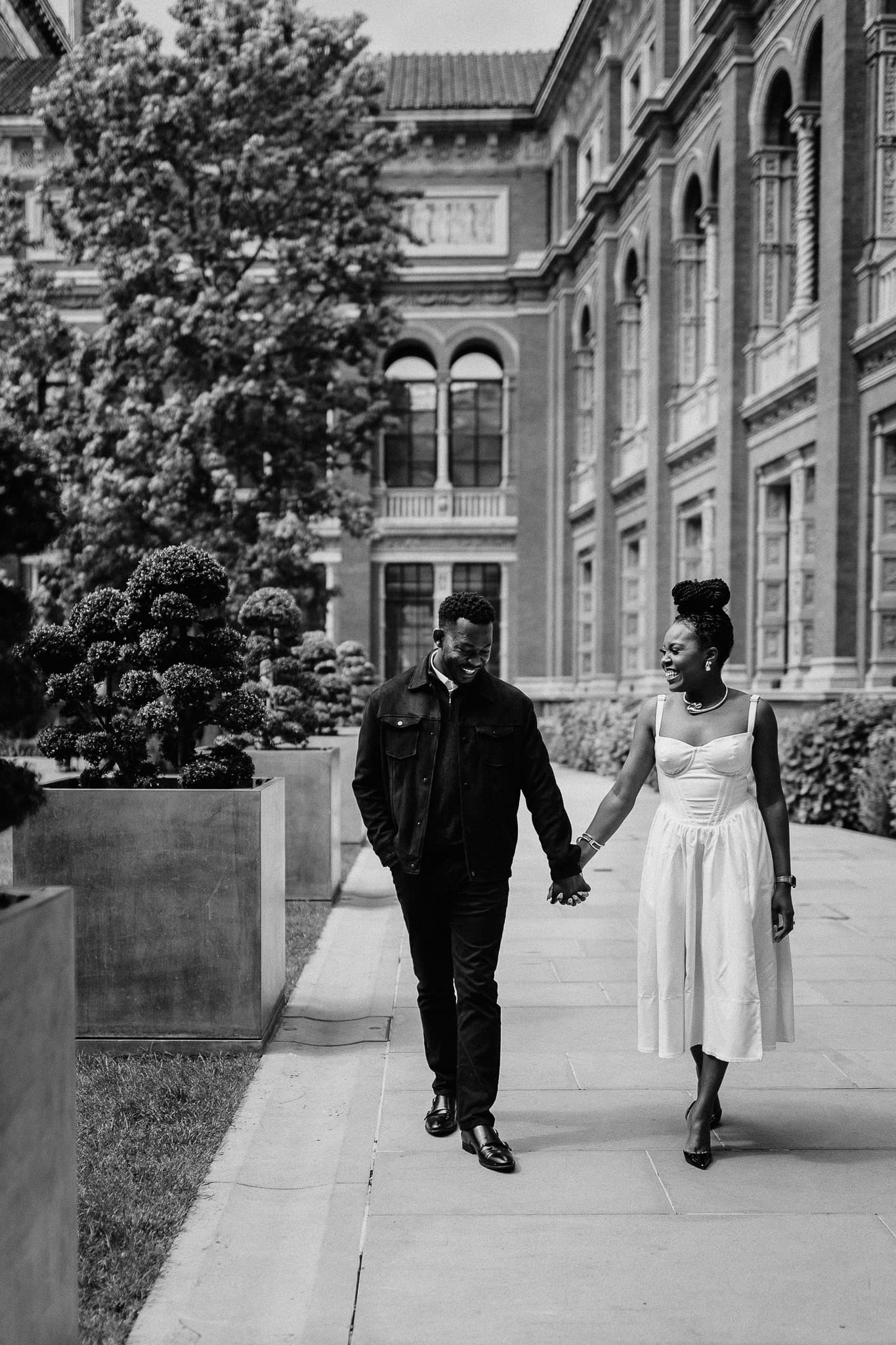 Couple holding hands, walking by a historic building. Elegant date, black and white photo.