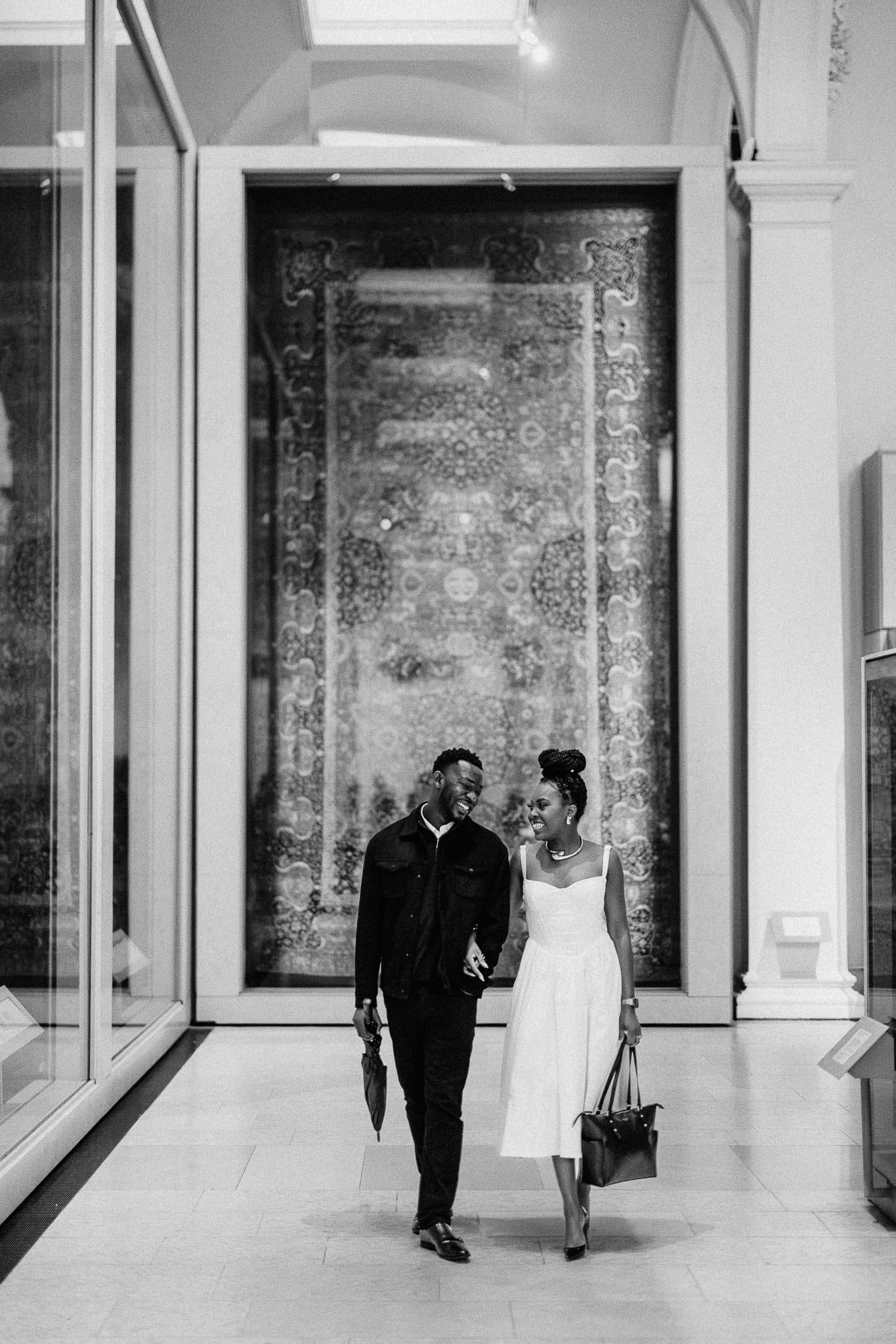 Couple walking arm in arm in a museum, smiling at each other.