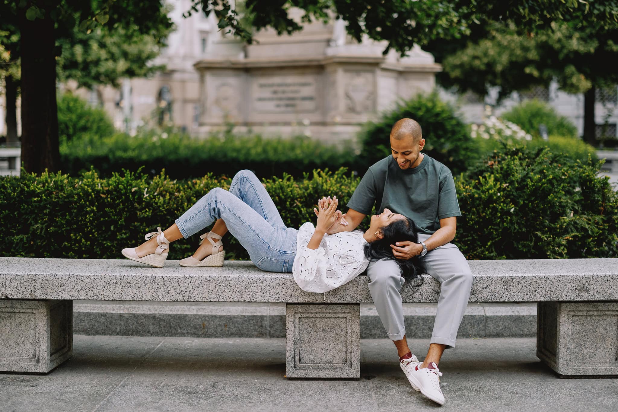 Couple relaxing on a bench in a park, woman lying with her head on man's lap, smiling.
