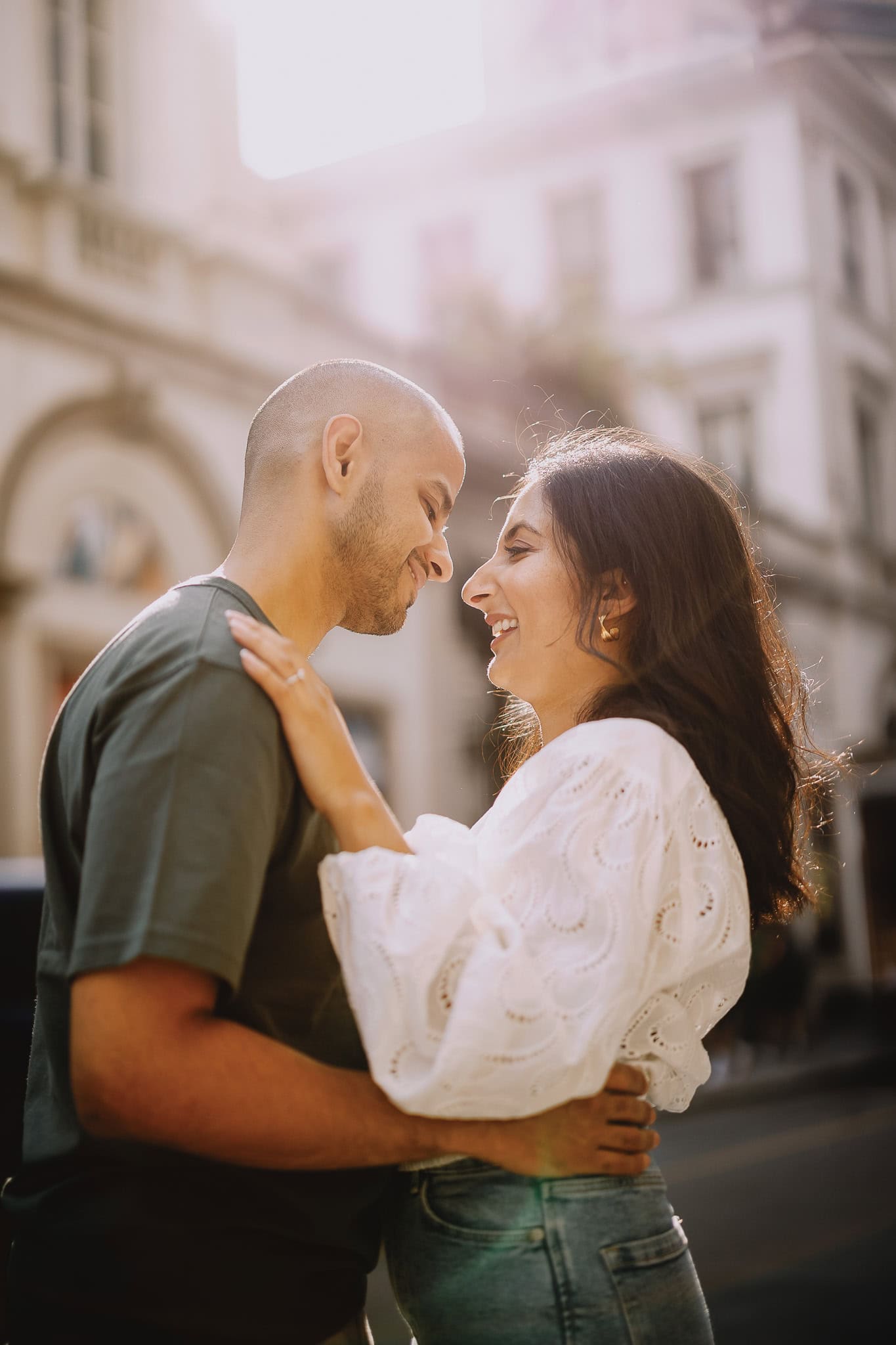 Happy couple embracing in city. Woman in white blouse, man in green shirt, smiling at each other.