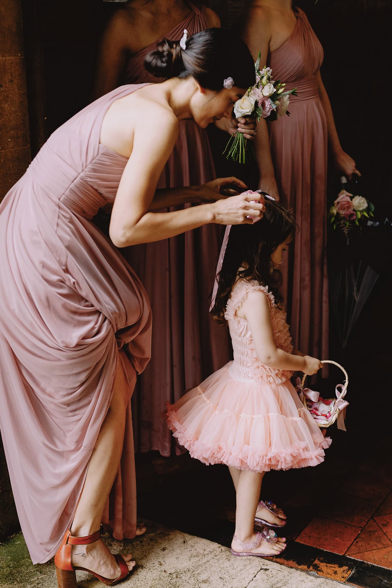 Woman adjusting flower girl's veil with bridesmaids in pink dresses behind