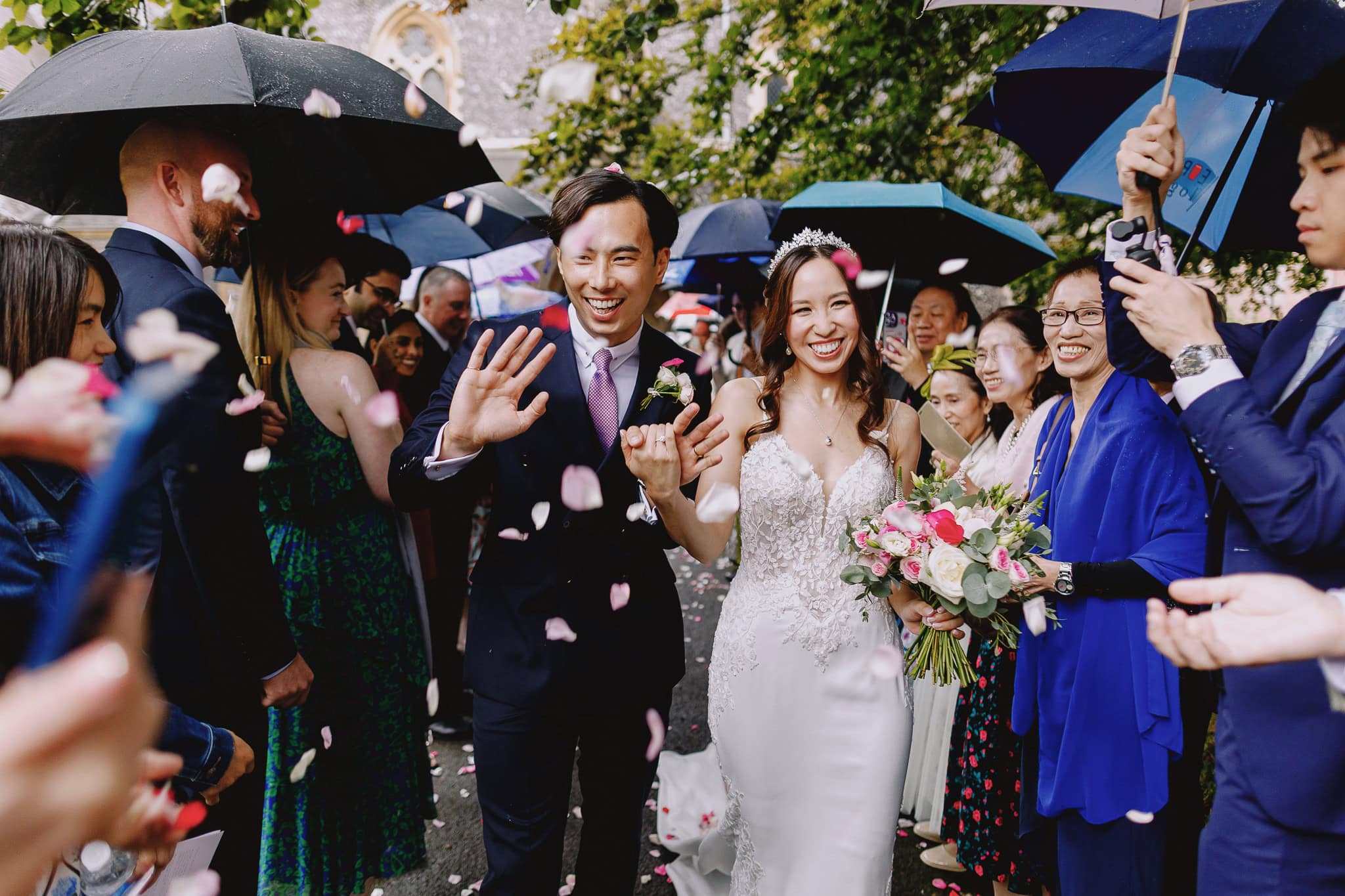 Happy couple walking through confetti under umbrellas after their wedding ceremony.
