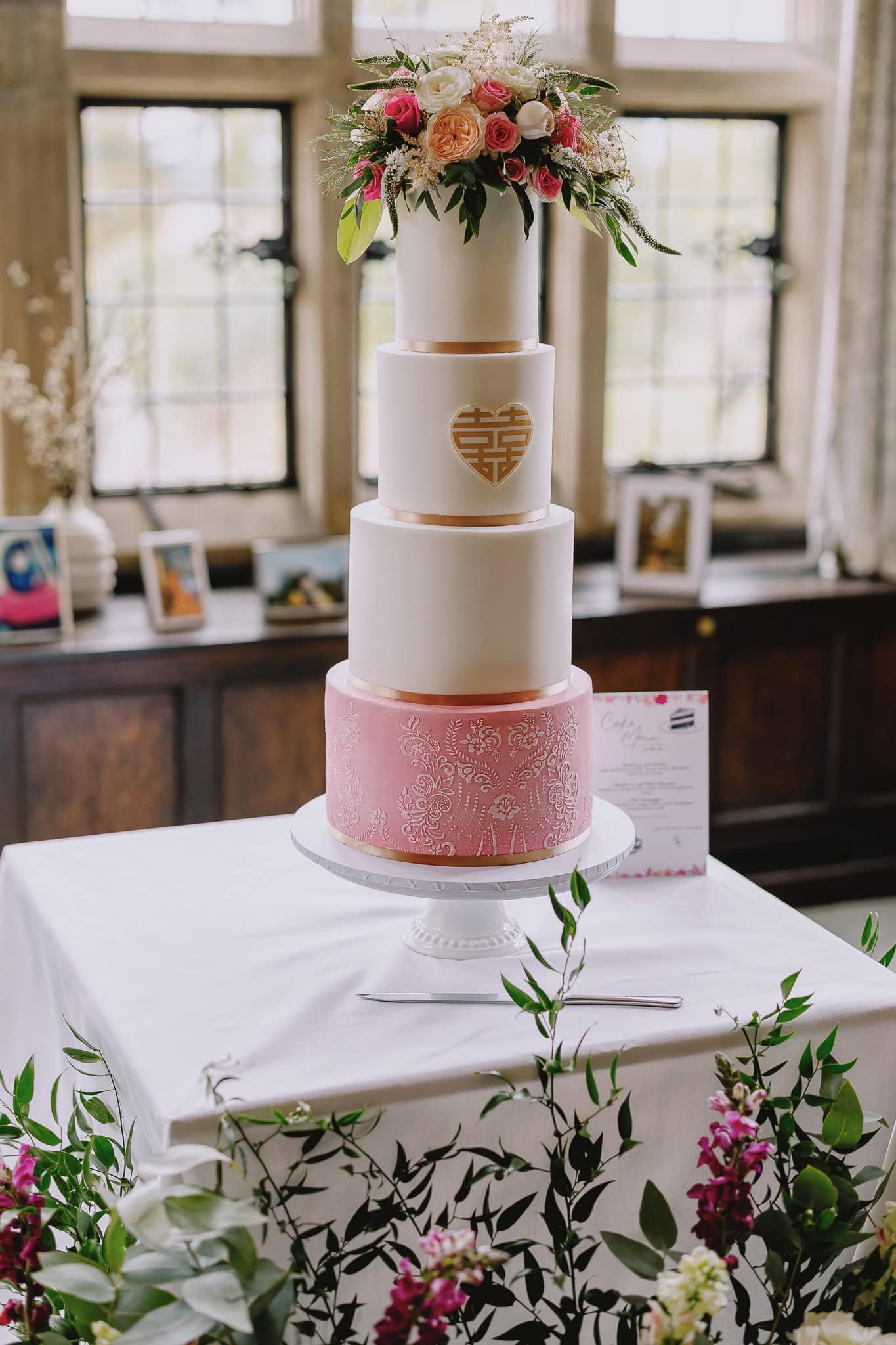 Elegant four-tier wedding cake with floral arrangement and Chinese symbol.