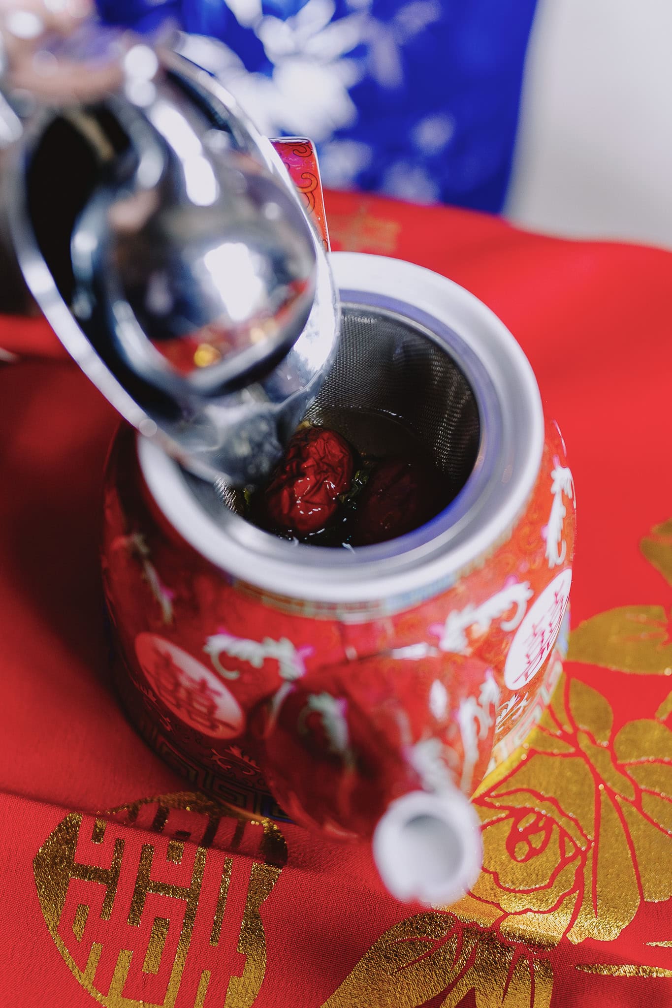Red Chinese teapot with jujubes being filled with hot water for a traditional tea ceremony.