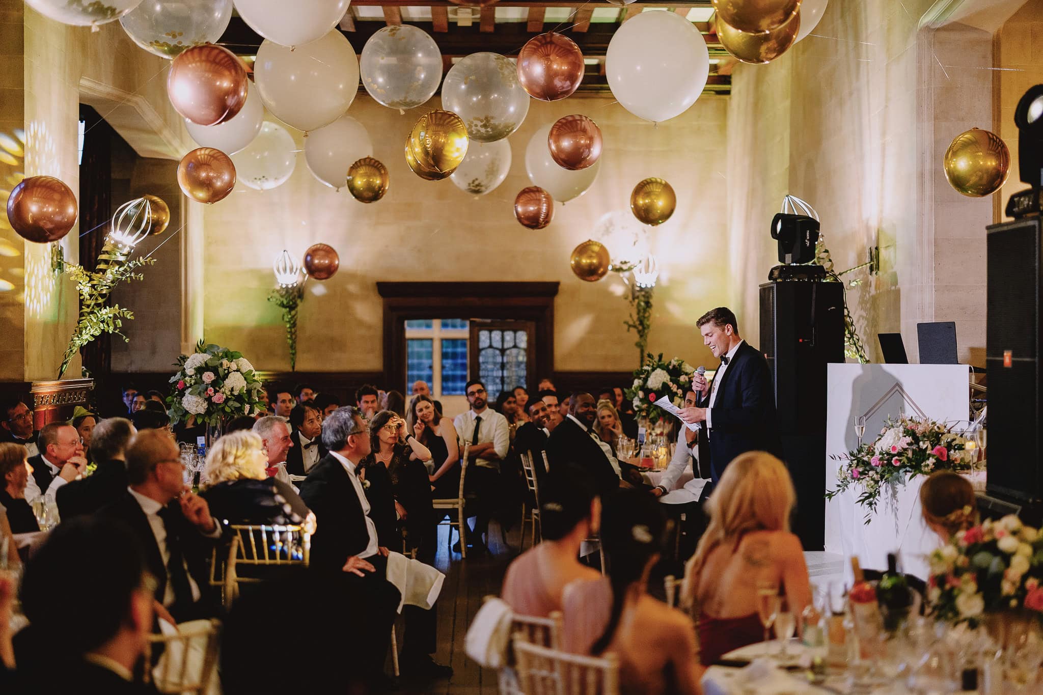 Groom giving a wedding speech under balloon decorations.