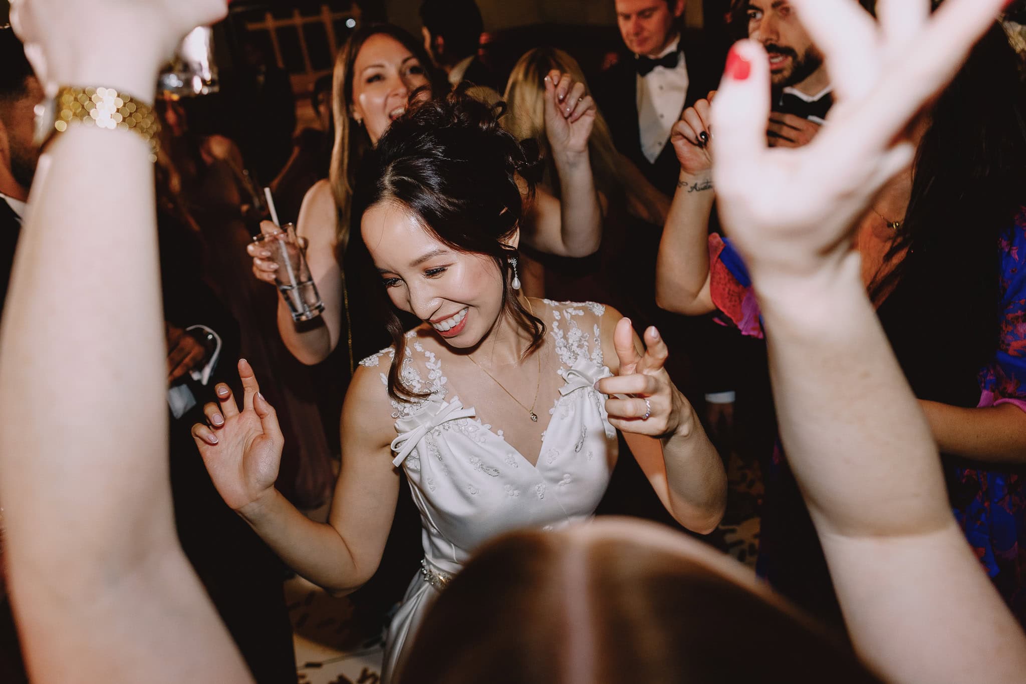Bride joyfully dancing at her wedding reception with guests raising their hands in celebration.