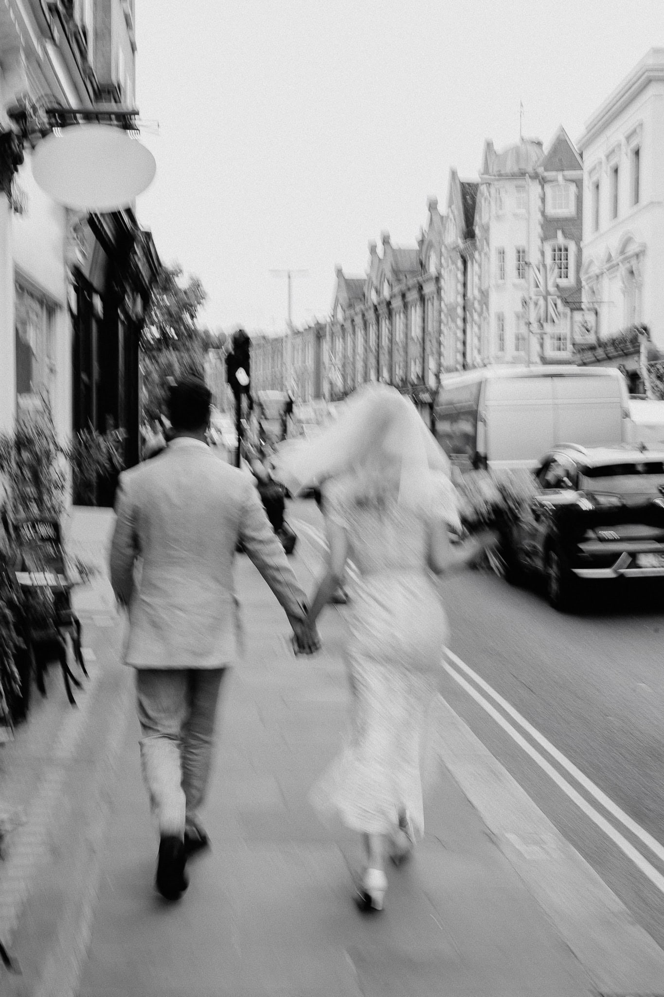 Newlyweds holding hands, running on a city sidewalk in London. Wedding photo.