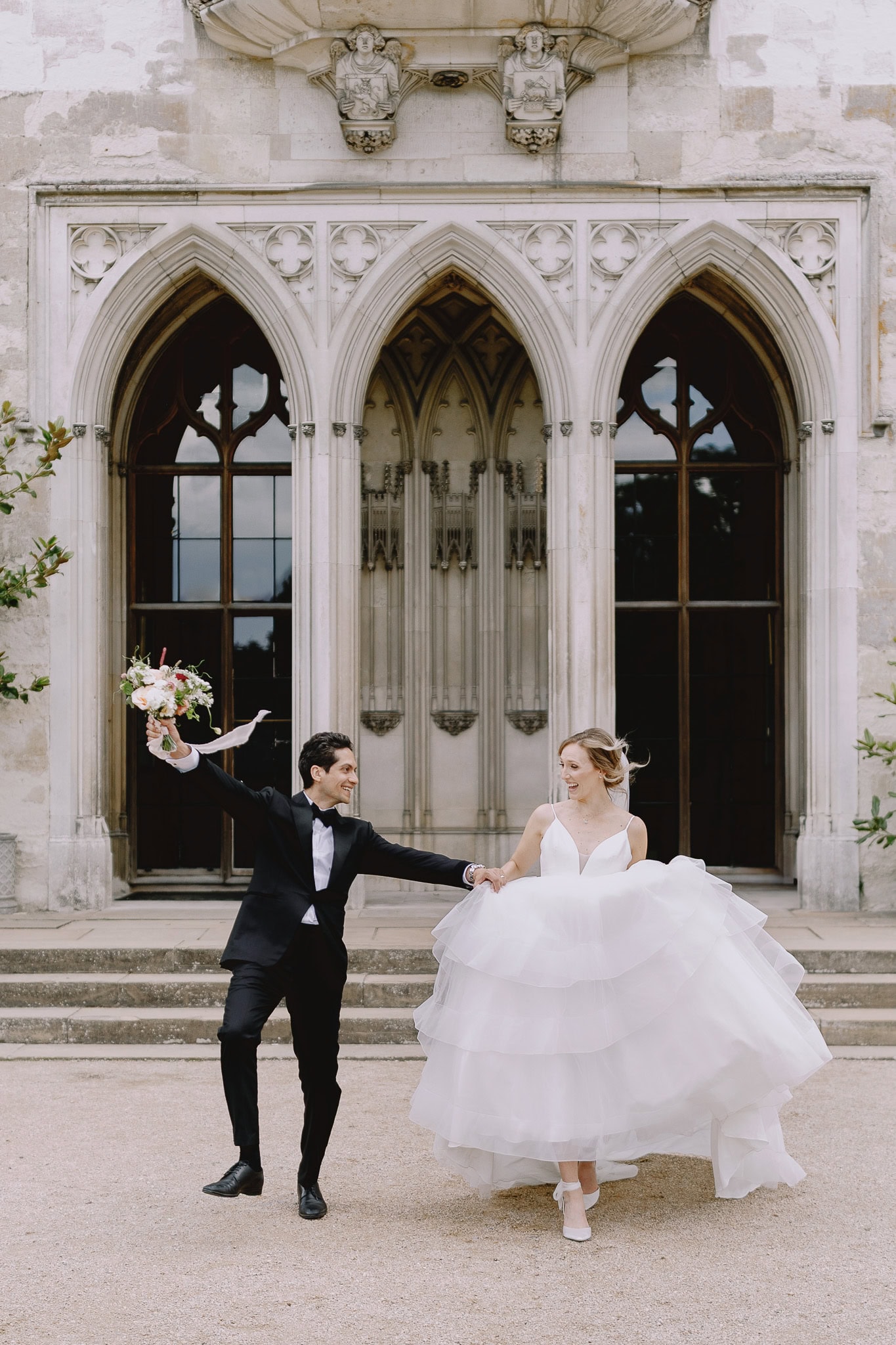 Editorial wedding photography: Bride and groom dancing joyfully in front of a grand building.