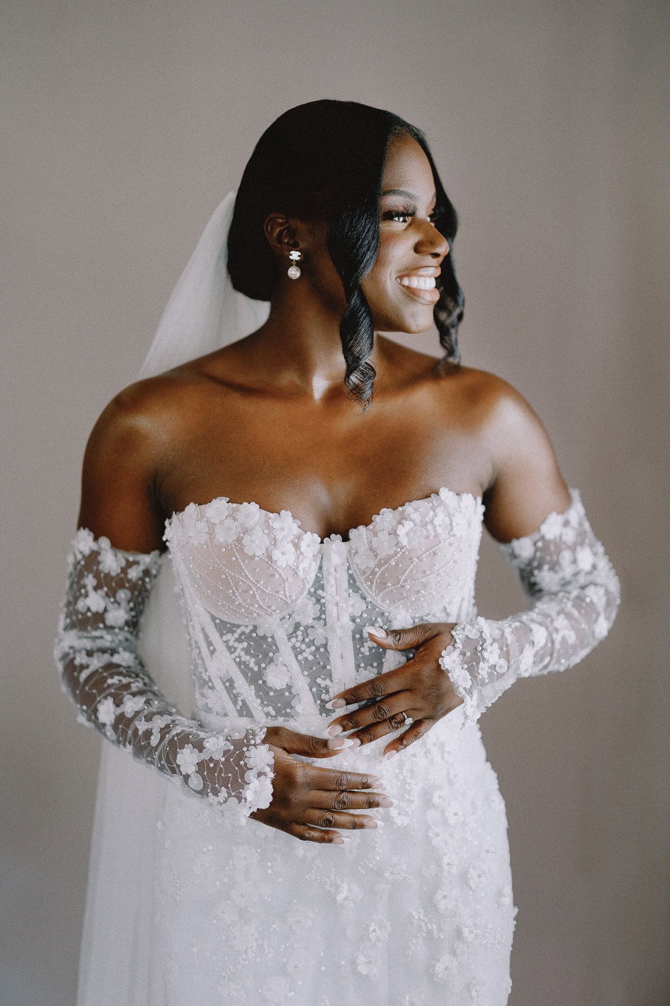 Editorial wedding photography: Bride in a white lace gown with sheer sleeves smiles.